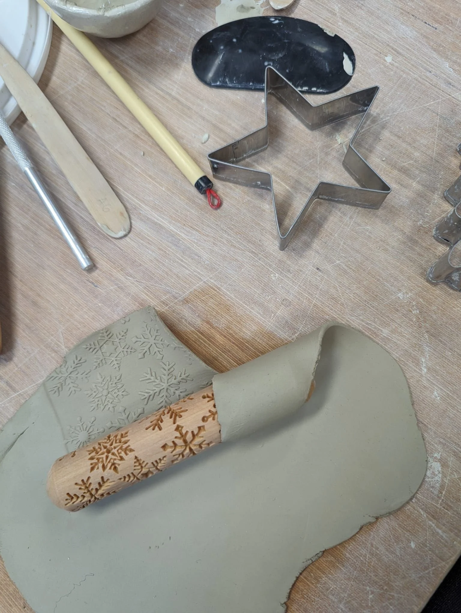 Baking tools on a wooden surface, including a star-shaped metal cookie cutter, silicone molds with snowflake patterns, a rolling pin, and a knife.