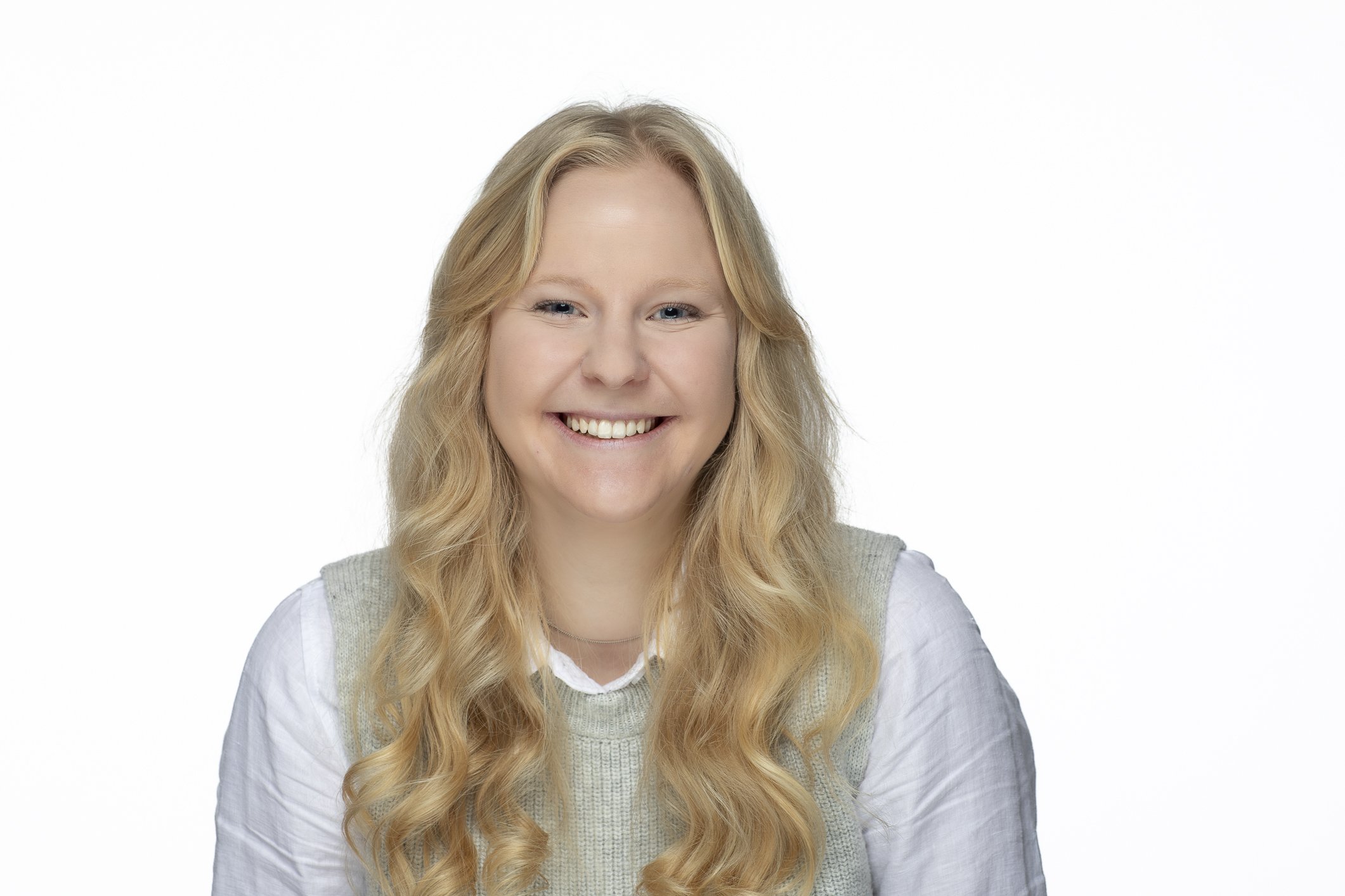 Portrait of a young woman with long blonde hair, smiling, wearing a light gray sweater over a white shirt, against a plain white background.