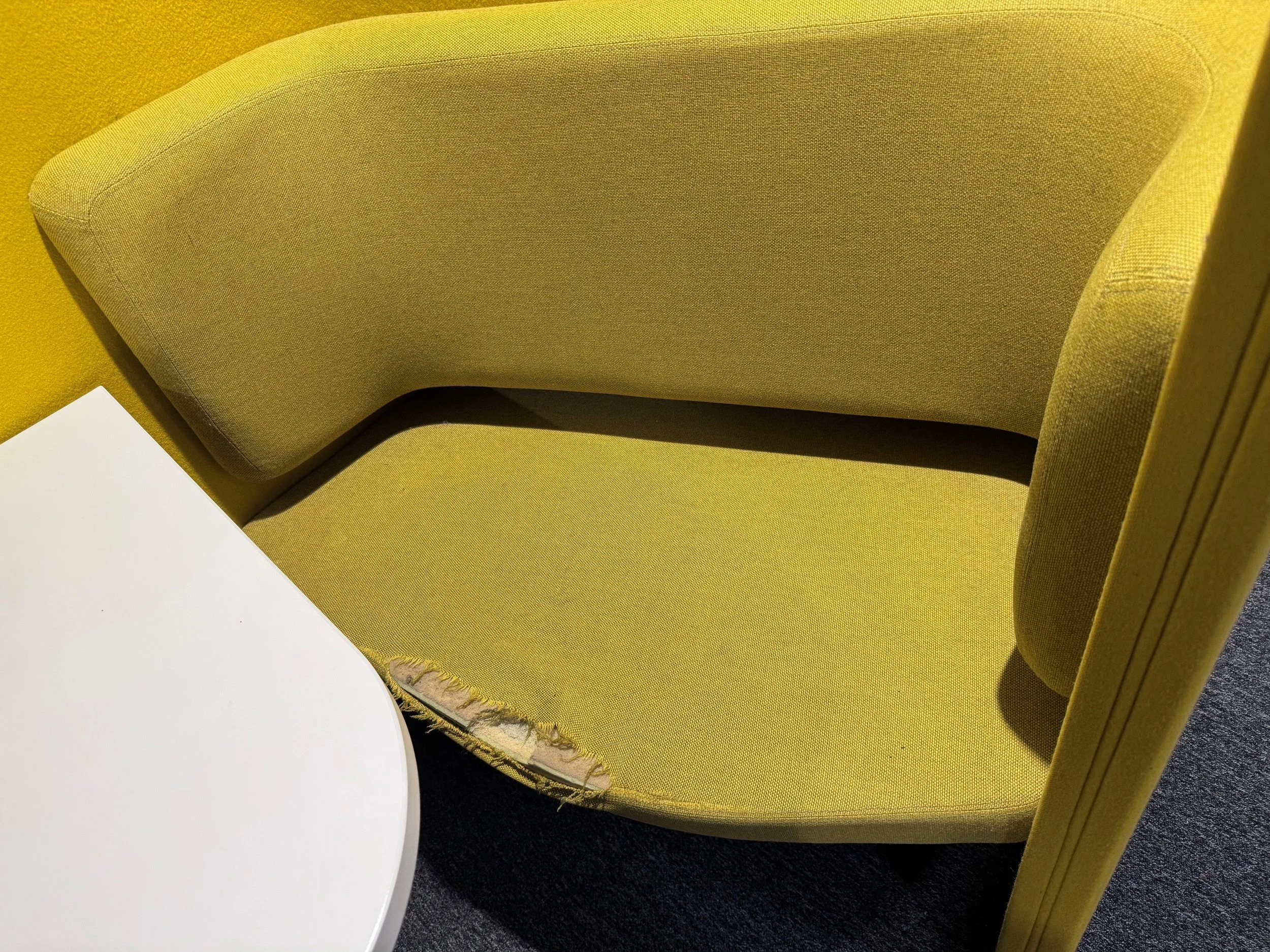 A yellow upholstered chair with a curved backrest next to a white round table on a dark carpeted floor.