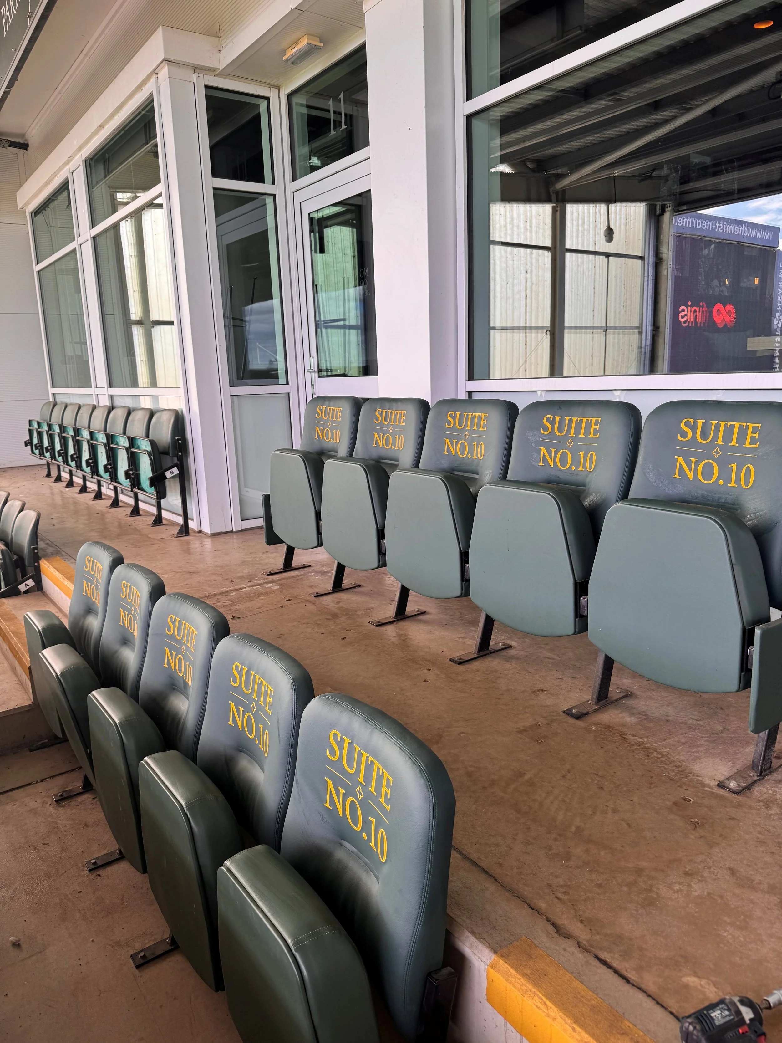 Row of seats in a waiting area, with some labeled 'SUITE NO.10' and others empty, next to a large glass window showing an indoor space and a sign for 'infinite'