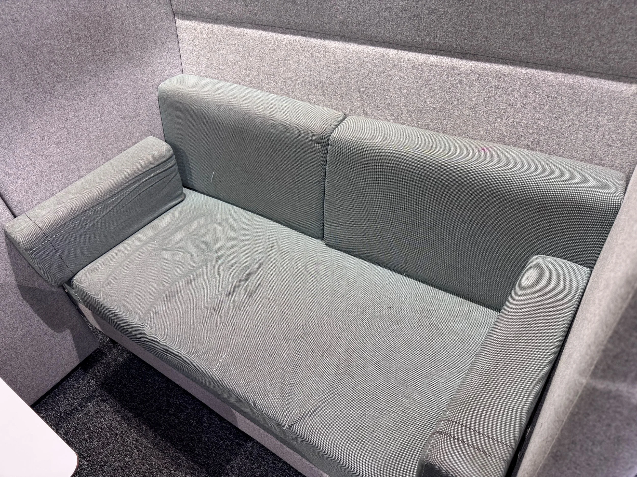 Gray fabric sofa with armrest in a room with gray carpeted walls and a white side table.
