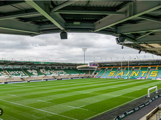 Empty rugby stadium with green field, white lines, and seating with 'SAINTS' written in yellow.