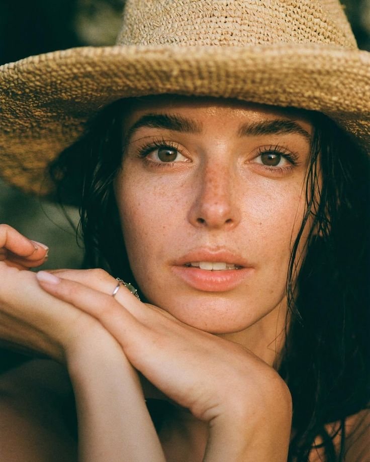 Woman with natural skin and freckles wearing a straw sun hat.