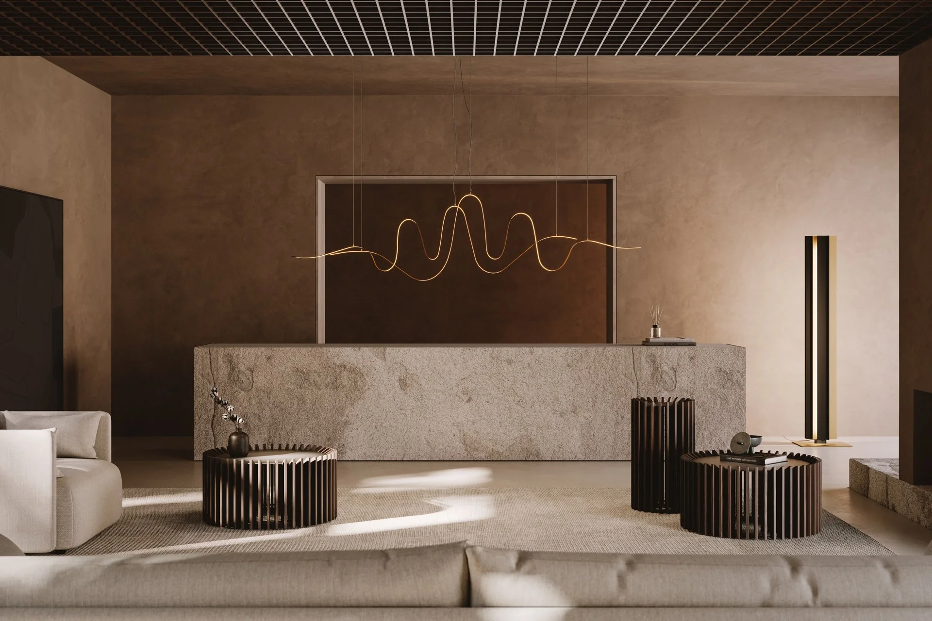 Modern living room with beige walls, a textured beige sofa, black circular side tables, and a sleek standing lamp. A contemporary gold and black sculptural light fixture hangs from the ceiling above a stone counter or desk, with some decor items on it.