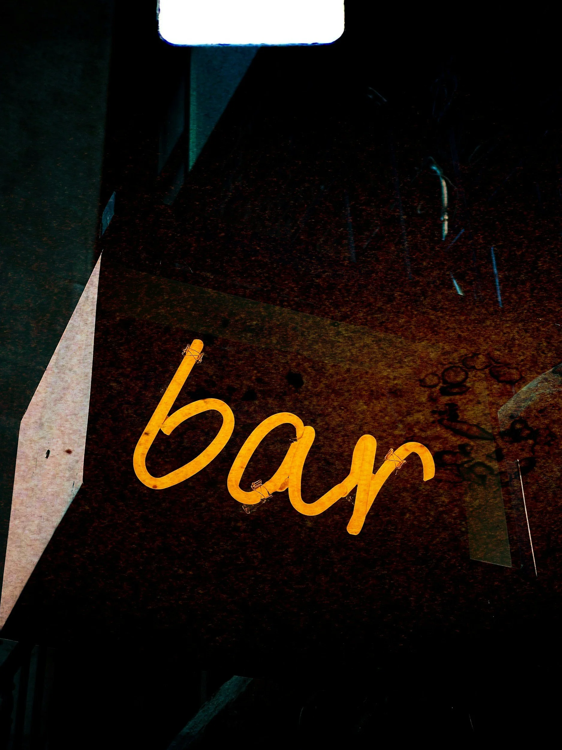 Neon sign spelling 'bar' in yellow, mounted on a dark exterior wall at night.