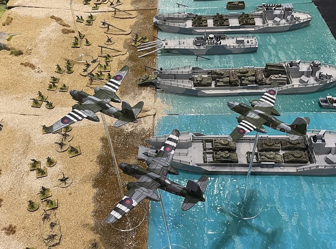 Miniature military battlefield with toy airplanes, warships, and soldiers, depicting a naval combat scene.