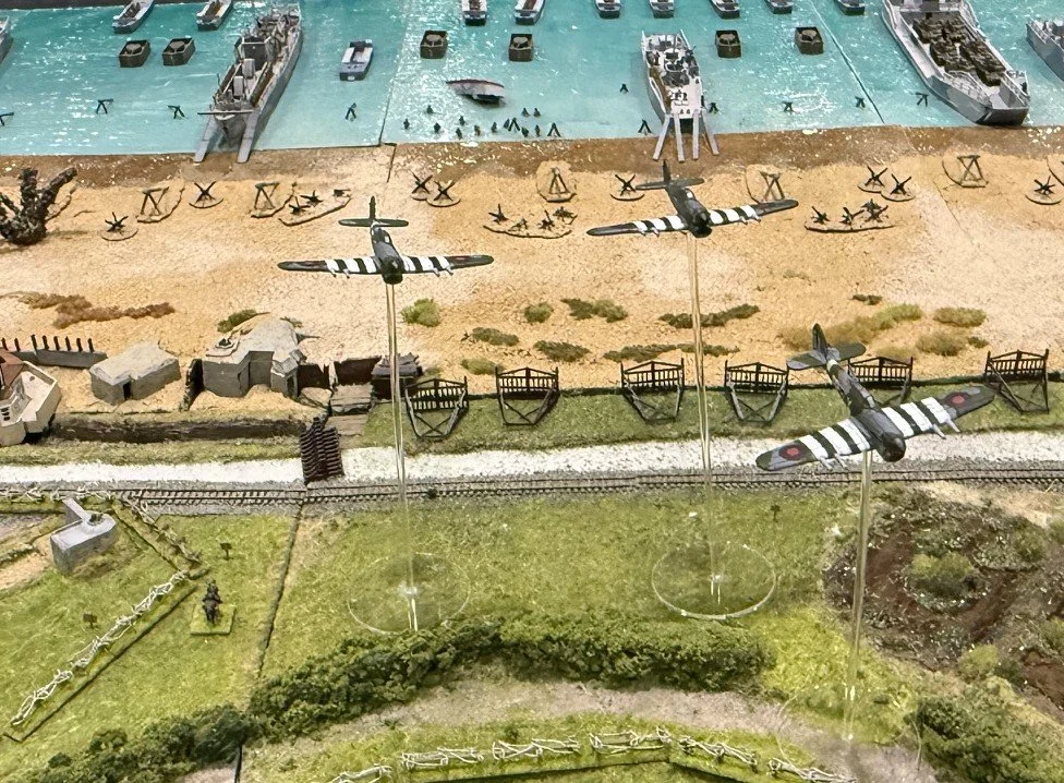 Model of a World War II battlefield with aircraft, ships, and military equipment.