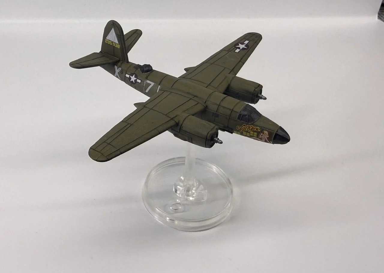 Model of a military airplane with a green camouflage paint scheme, displayed on a clear circular stand against a plain white background.