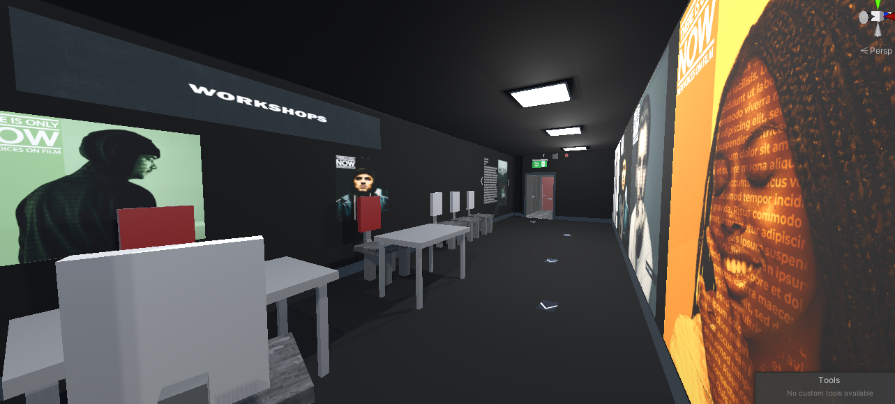A dark hallway with various posters and artwork on the walls, labeled 'WORKSHOPS' on a sign overhead, with tables and chairs along one side, and a door at the end of the hallway.