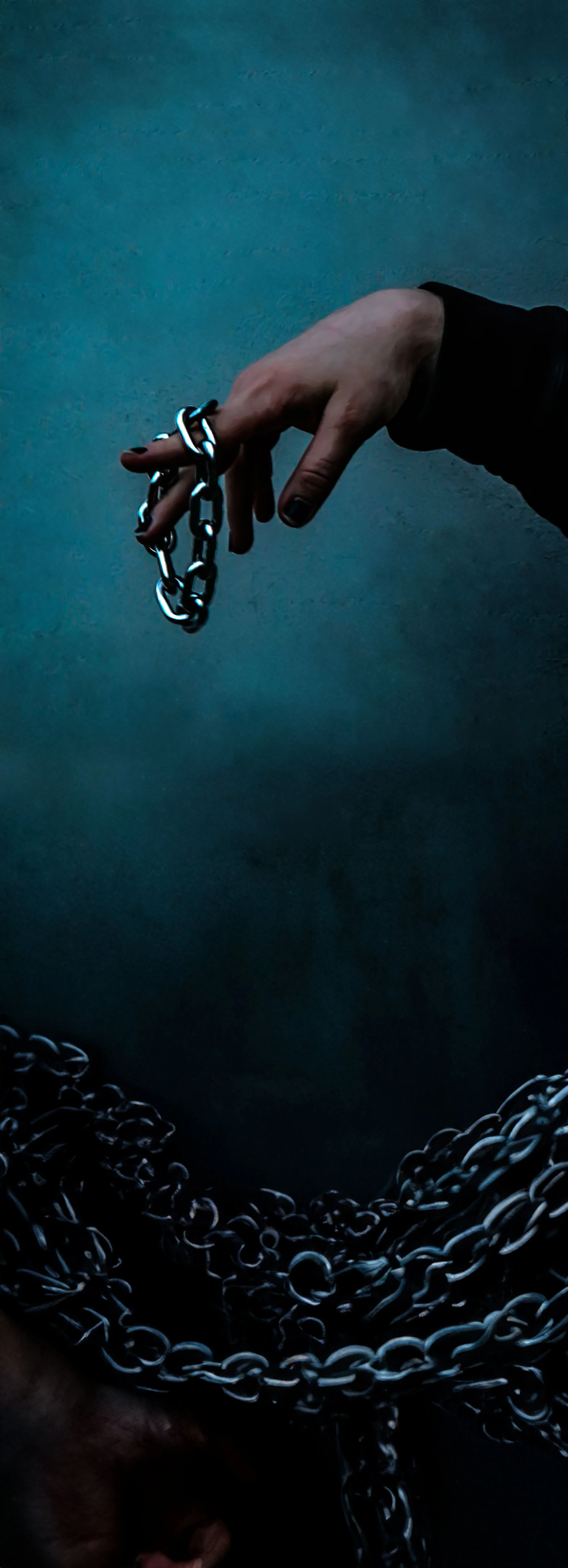 A person holding a black metal chain in front of a dark textured background, with a pile of similar chains at the bottom.