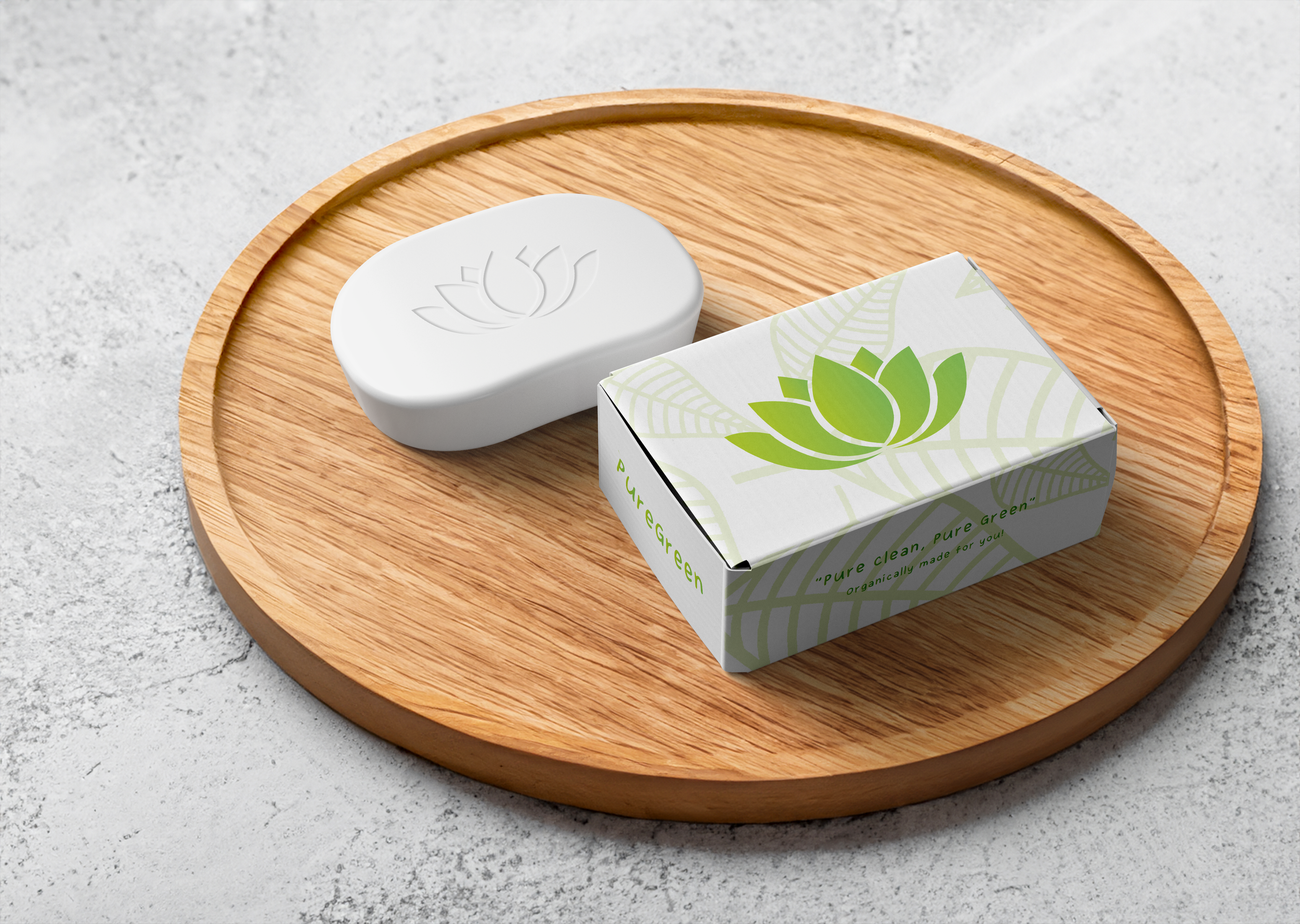 A white bar of soap with a lotus flower and leaf design embossed on top, placed on a round wooden tray, next to a box with a similar lotus and leaf design, on a light gray speckled surface.
