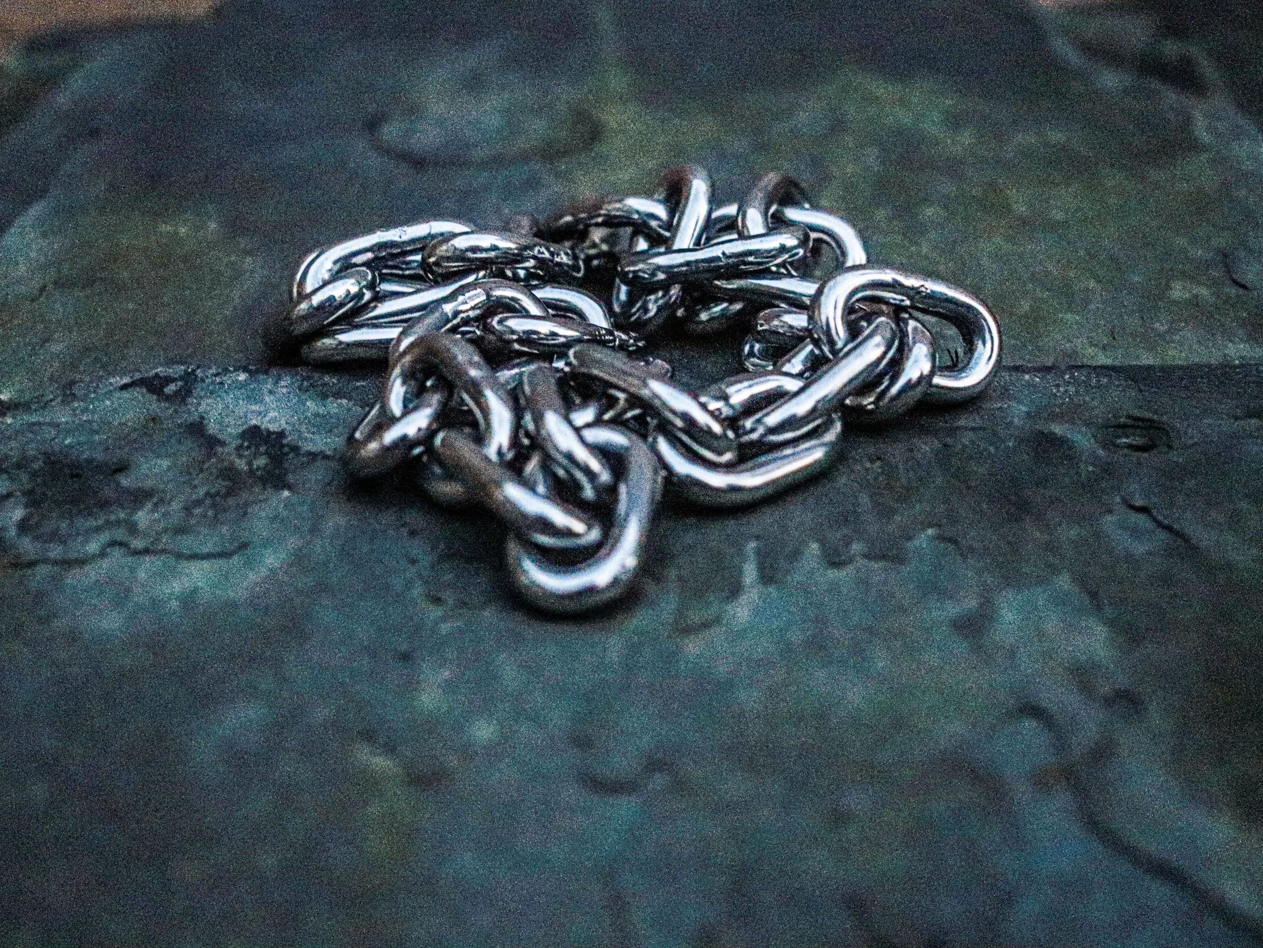 A close-up image of a tangled pile of metallic chains on a dark surface.