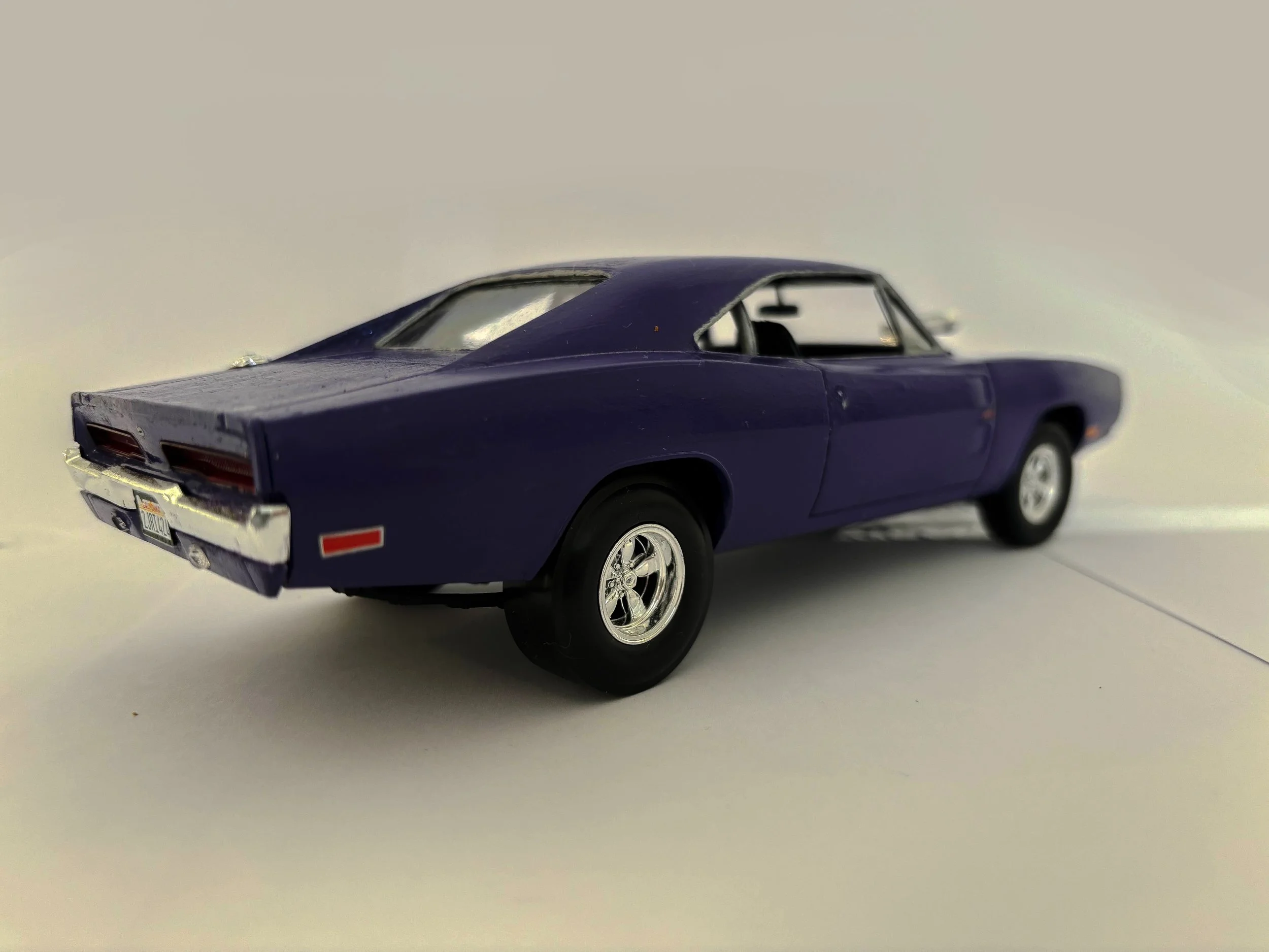 A purple model car 1969 dodge charger with silver wheels viewed from a low angle against a plain, light background.