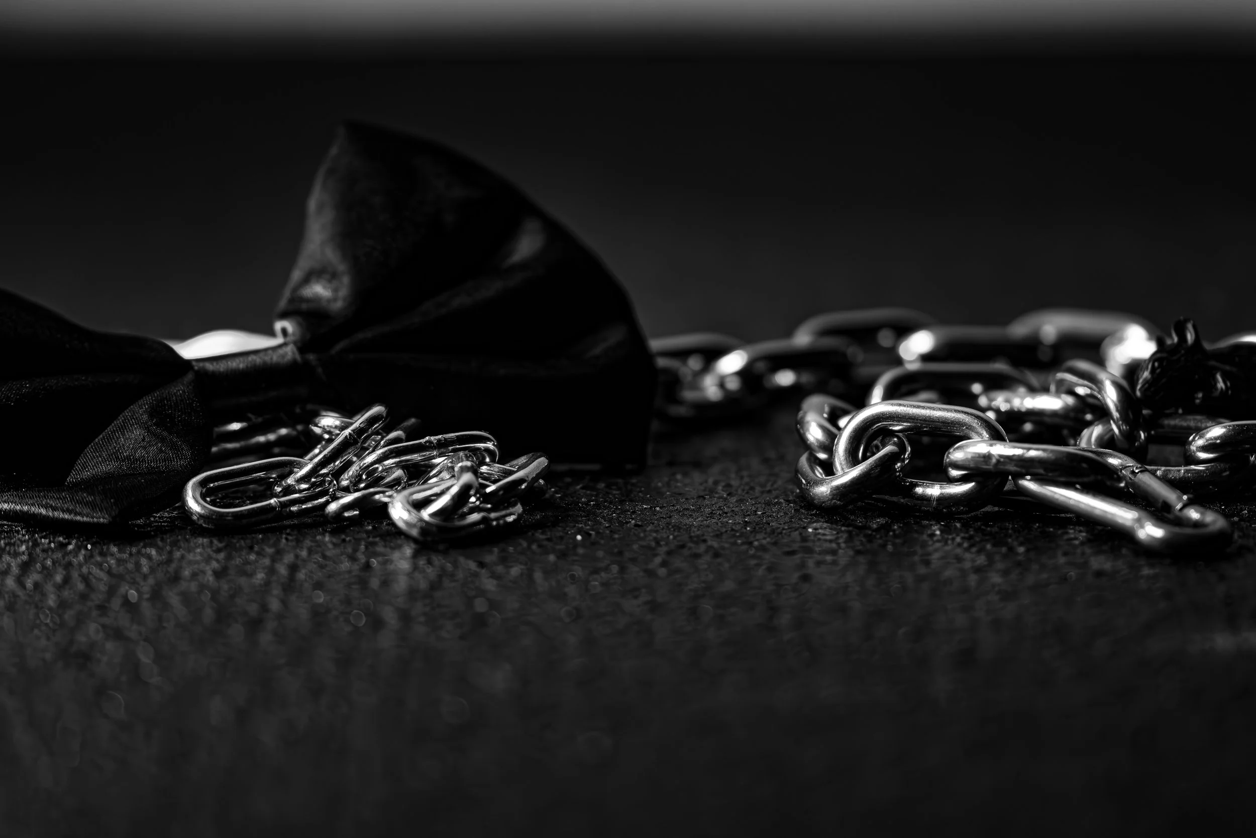 A black and white image showing a chain, a ribbon, and a small figurine on a dark surface.