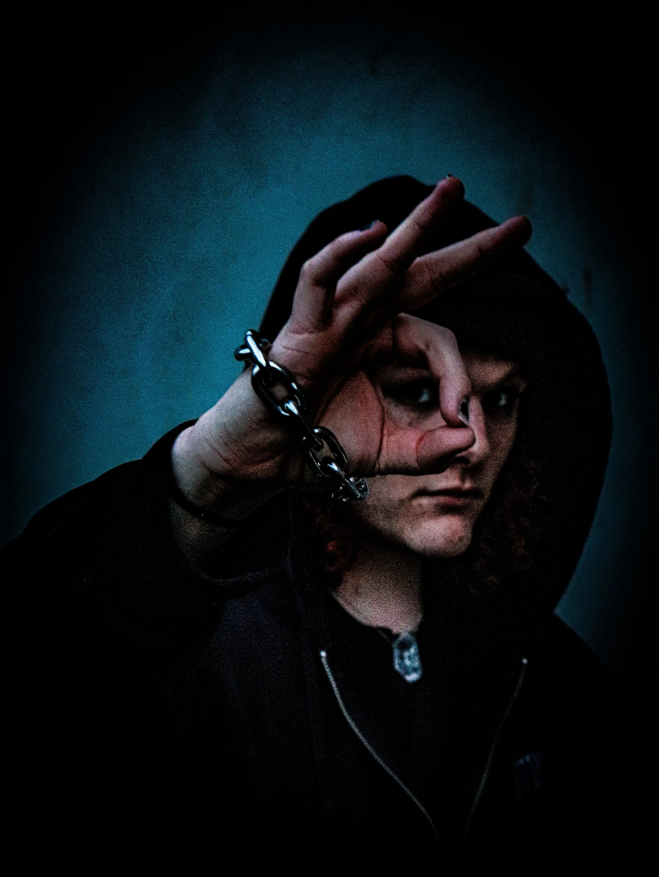 Close-up of a person with dark hair making a heart shape with their hands, wearing a black hoodie, against a dark background.