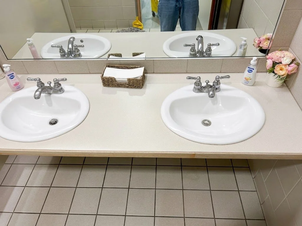 Commercial restroom cleaning showcasing a sparkling double sink vanity, rolled hand towels, and soap dispensers.
