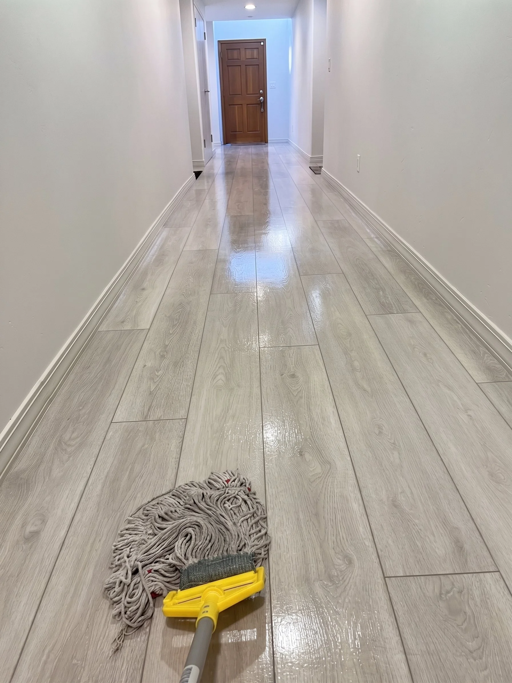 Professional floor cleaning services, showing a yellow mop on shiny beige hardwood floors in a spacious living room.