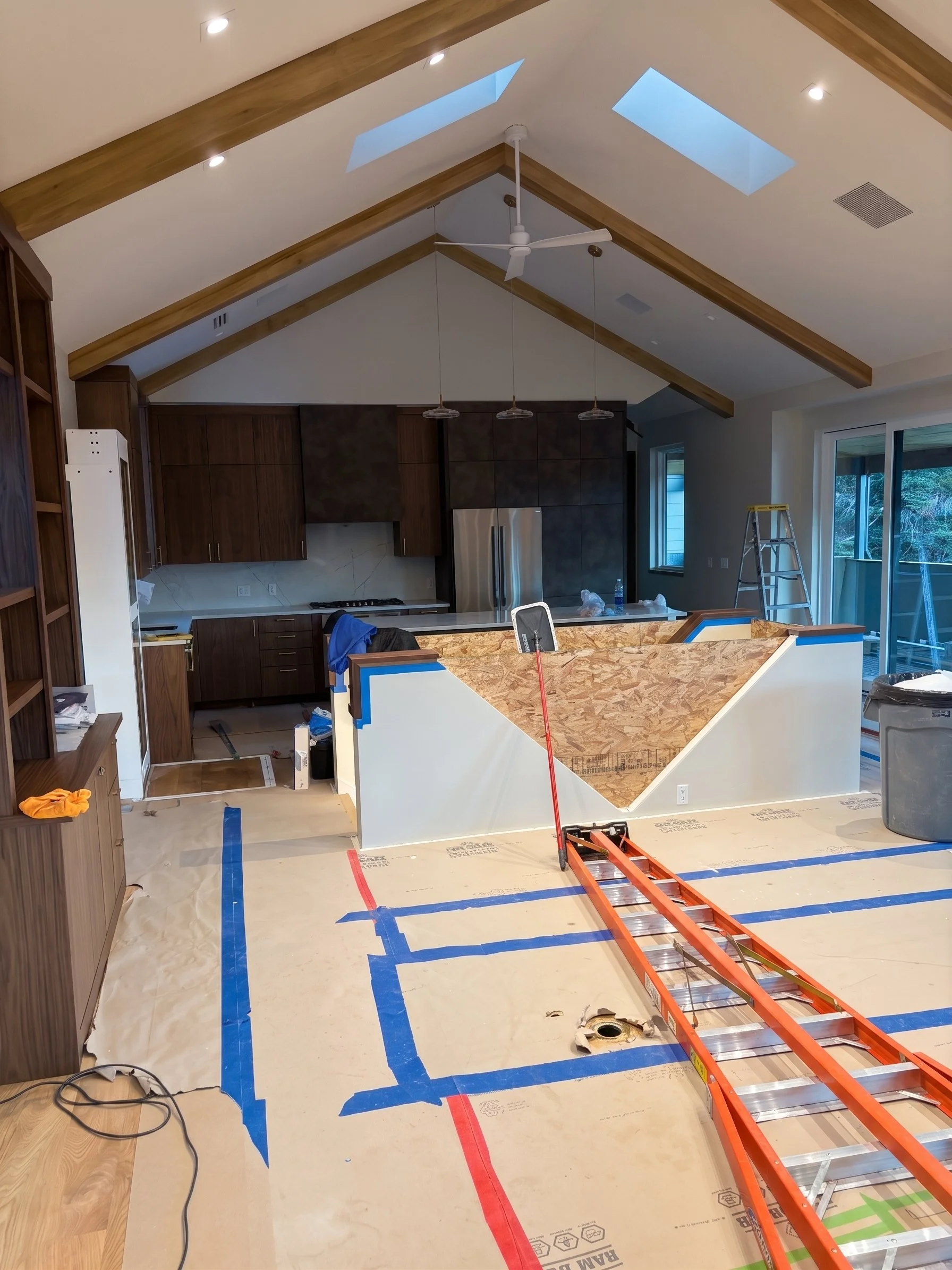 Kitchen renovation cleaning in progress, featuring a partially installed island, ladder, and vaulted ceiling with skylights.