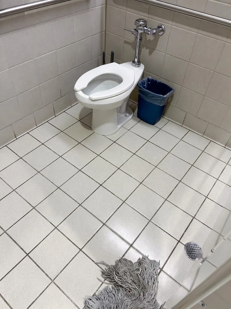 Commercial bathroom cleaning services showing a freshly mopped public restroom with a toilet and floor drain.