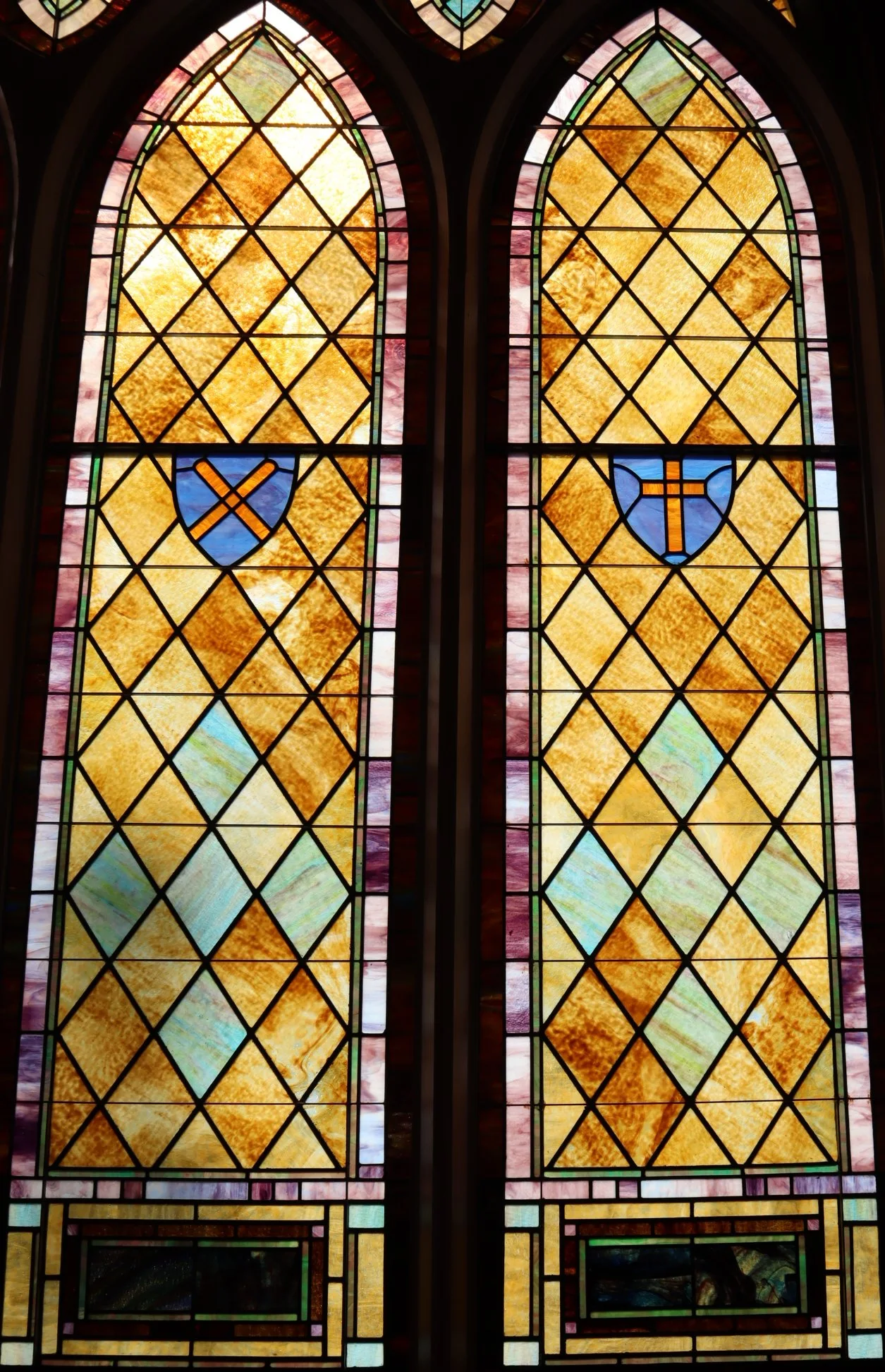 Stained glass windows with geometric patterns and shields with orange symbols, possibly representing a religious or historical context.