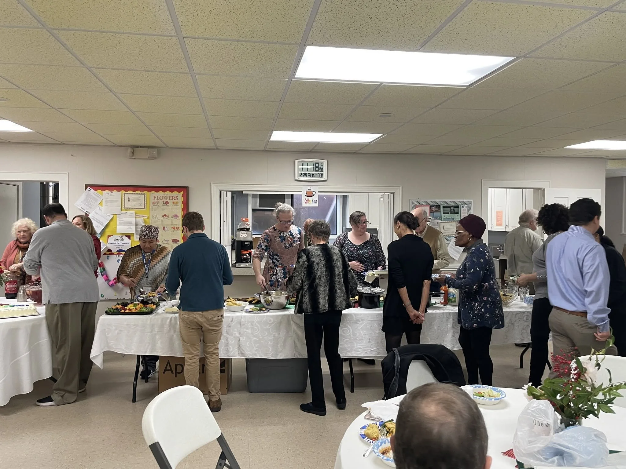 People gathered around a long table with food at an indoor social event or gathering.