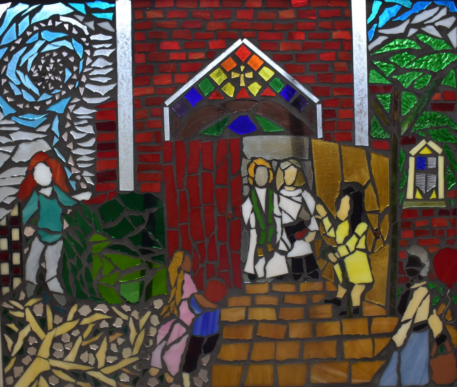 A colorful stained glass window depicting a family scene in front of a house with a red door, including children, a woman, and a man, surrounded by trees and decorative elements.