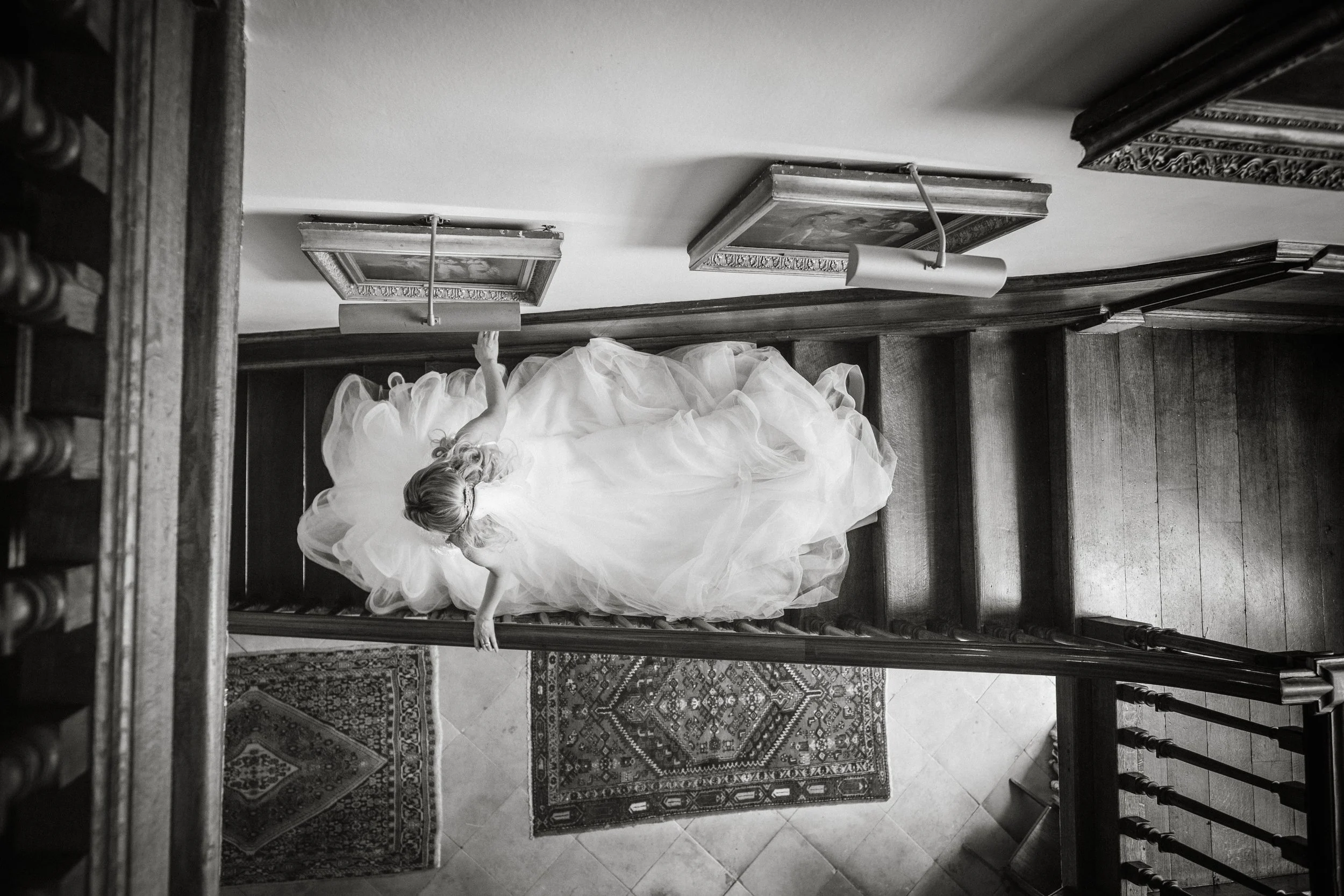 A woman in a large, flowing gown with ruffled layers is descending a staircase in an elegant, vintage-style interior.