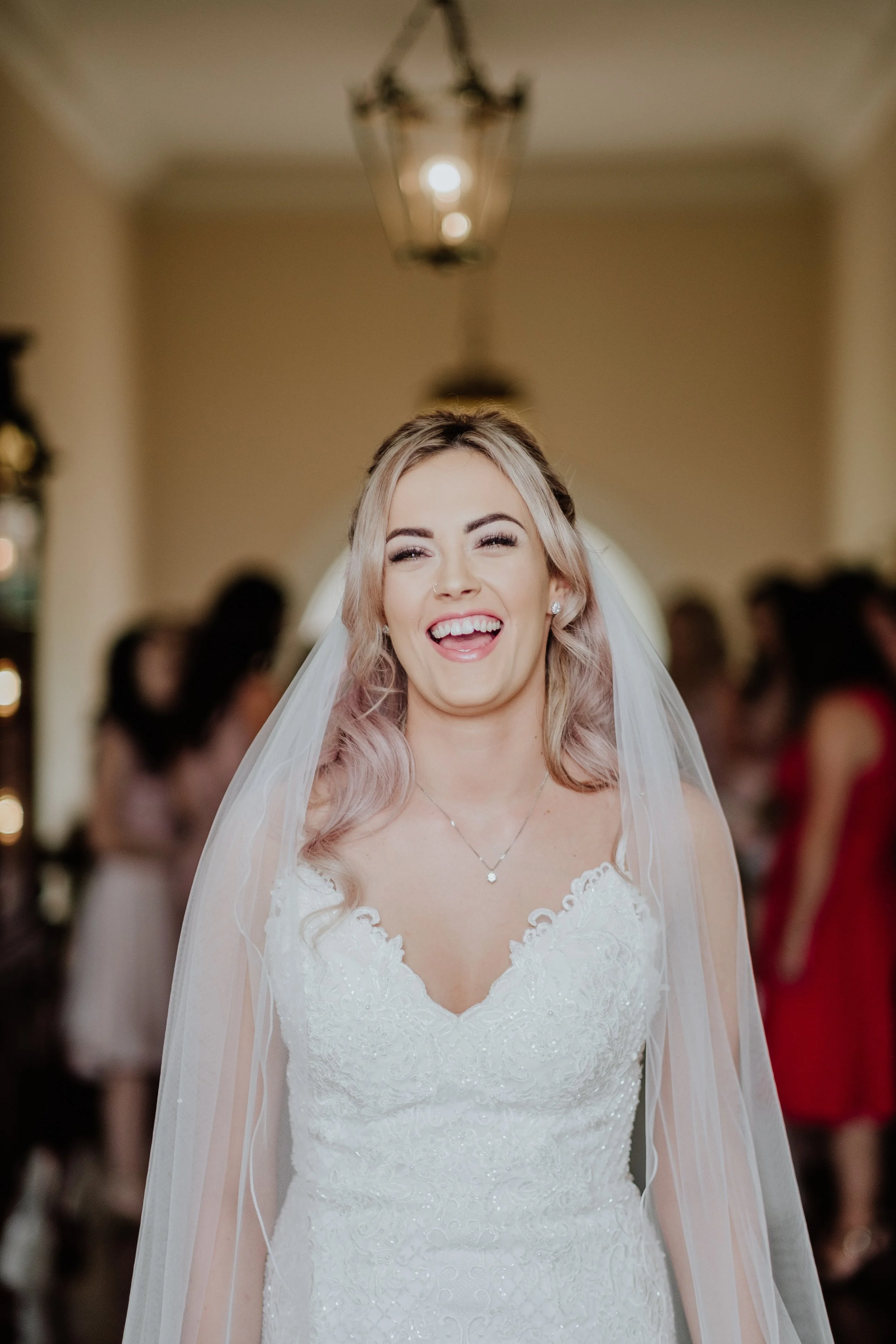 Smiling bride with blonde hair in a white wedding dress and veil, indoors at a wedding reception.