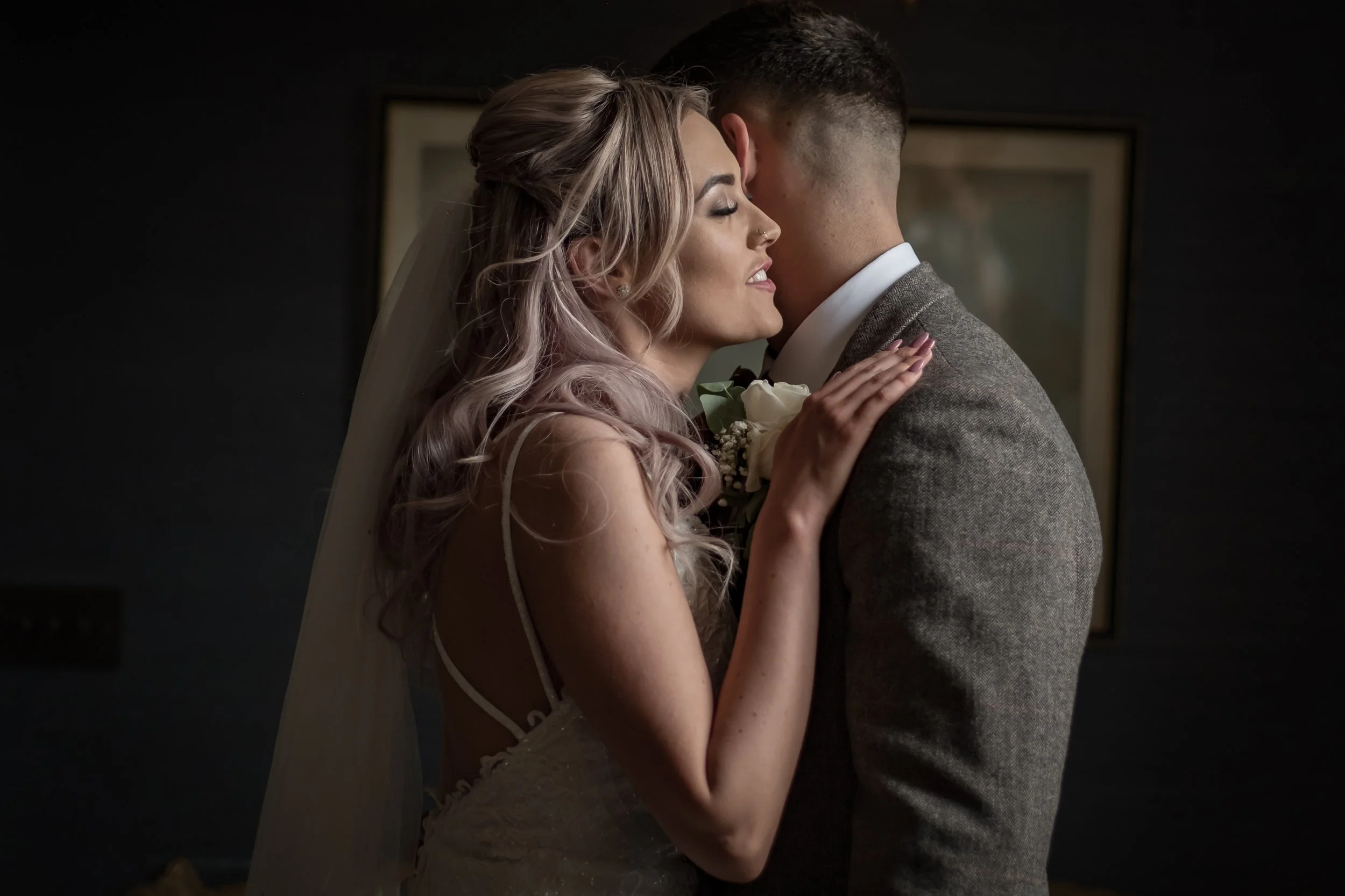 A bride and groom sharing a close embrace during their wedding, with the bride smiling with her eyes closed and the groom facing away from the camera.