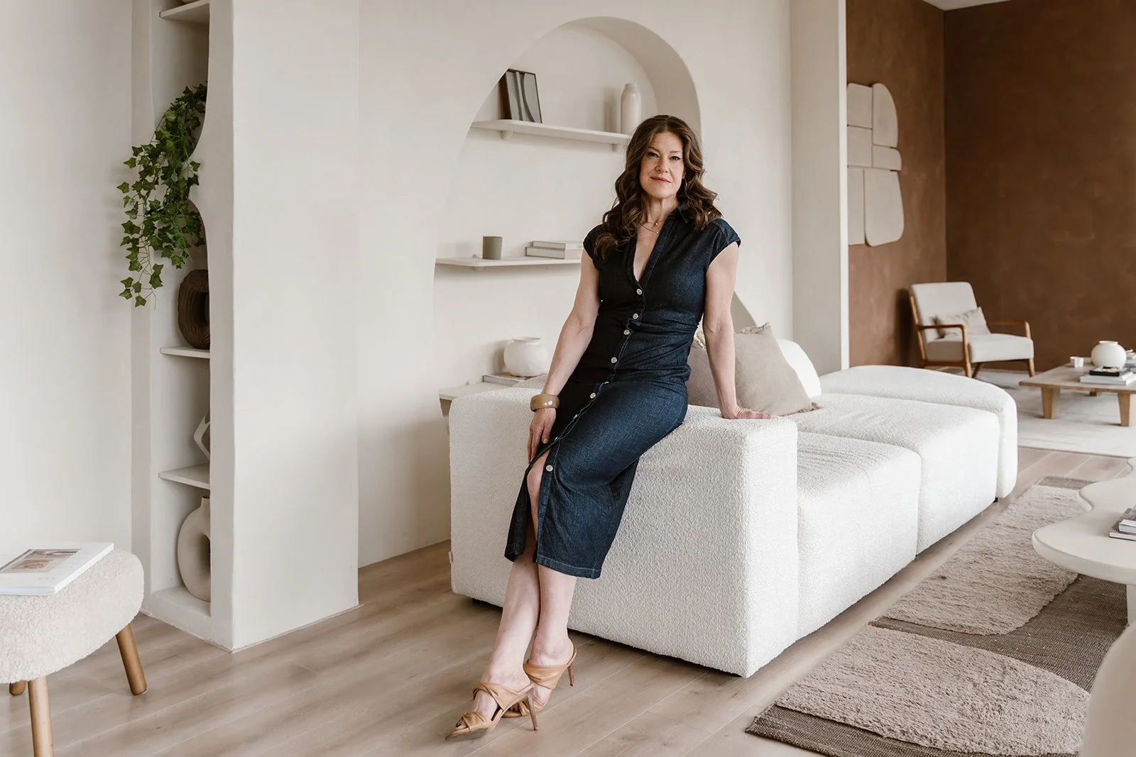 Woman sitting on a white couch in a modern living room with a neutral color palette.
