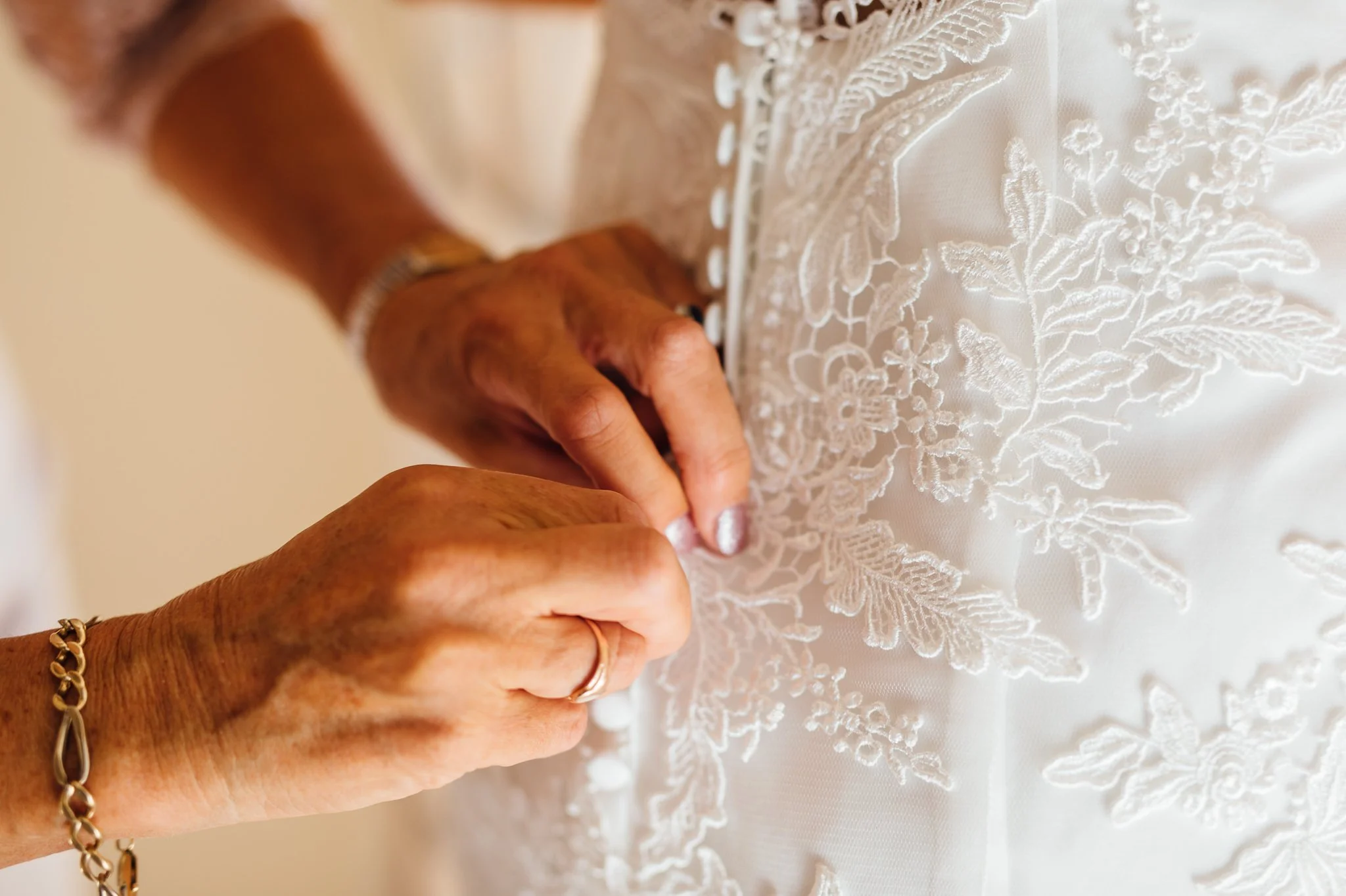  Closeup of the back of the Bride’s dress being buttoned up  