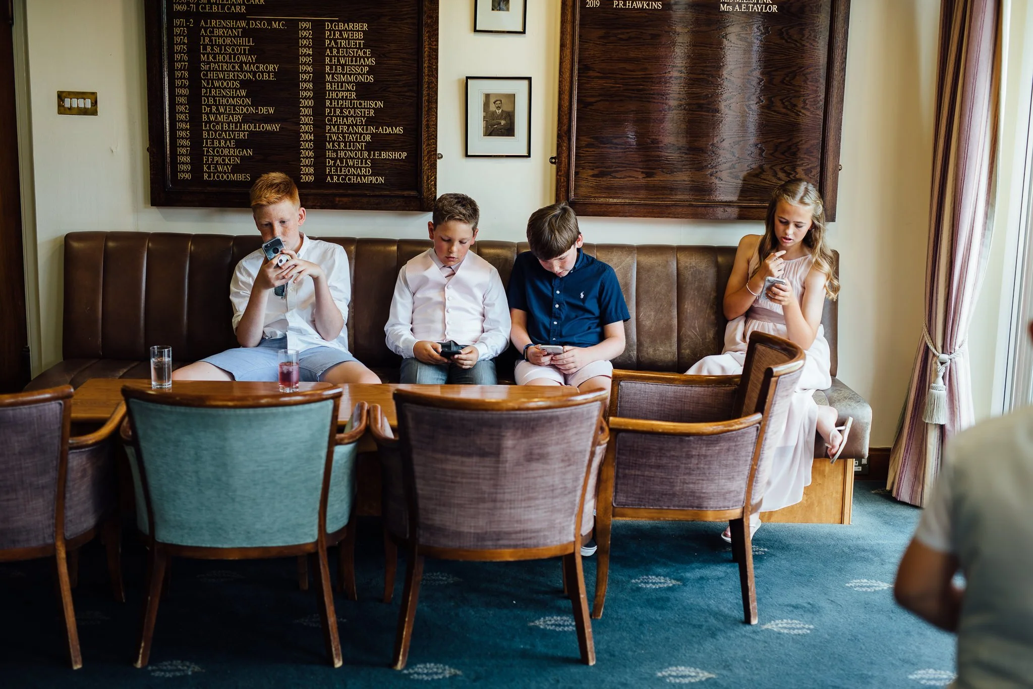  Young wedding guests stare at their phones  at Walton Heath Golf Club Surrey 