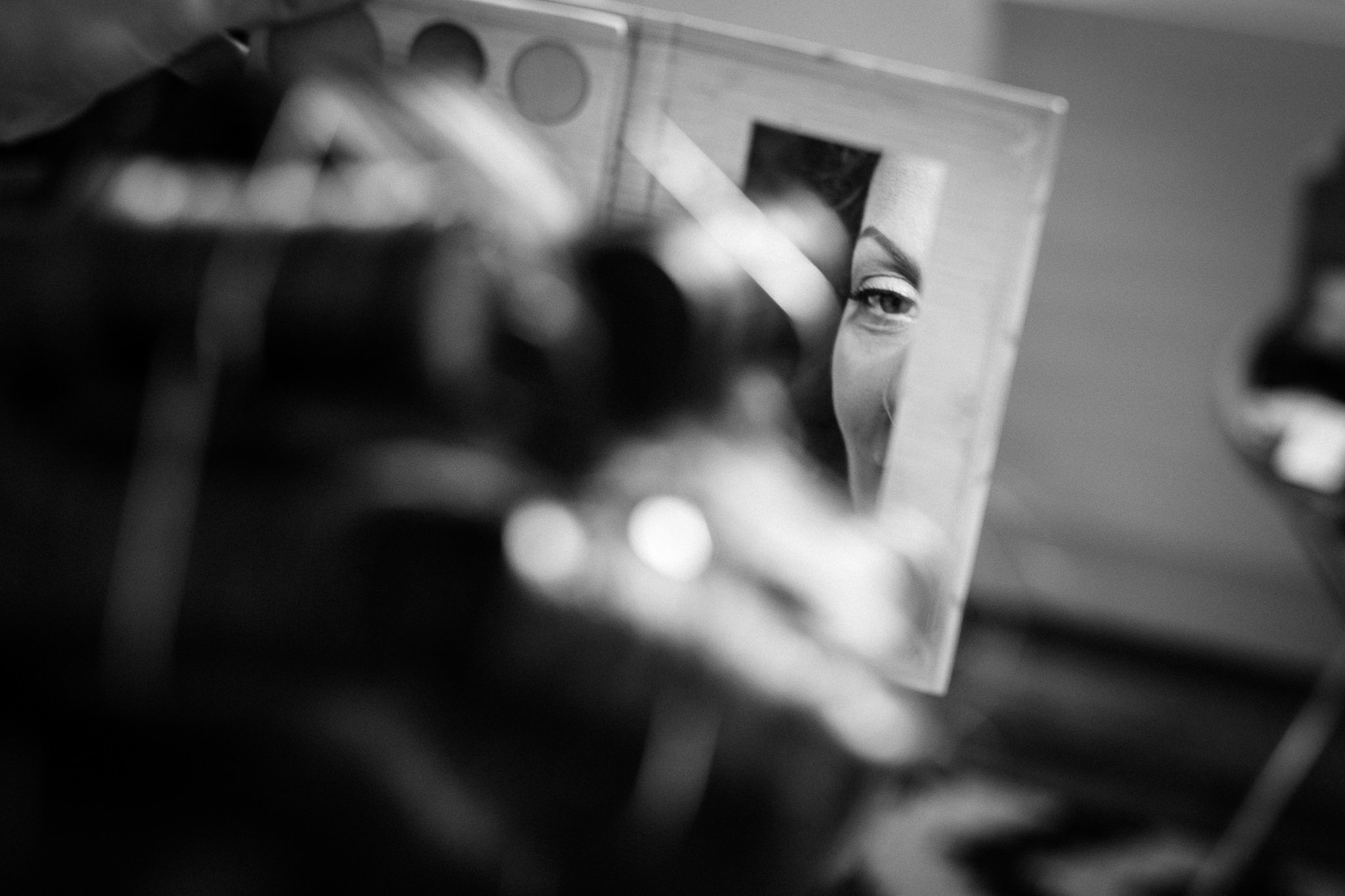  Bride doing her eye makeup whilst looking in a mirror on her wedding day 