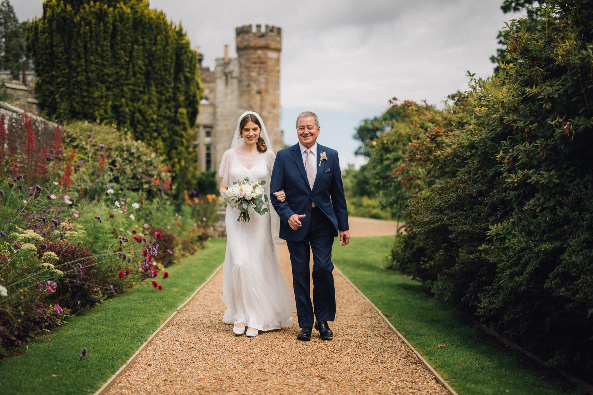  Bride and the Father of the Bride walk along a gravel path to the ceremony 