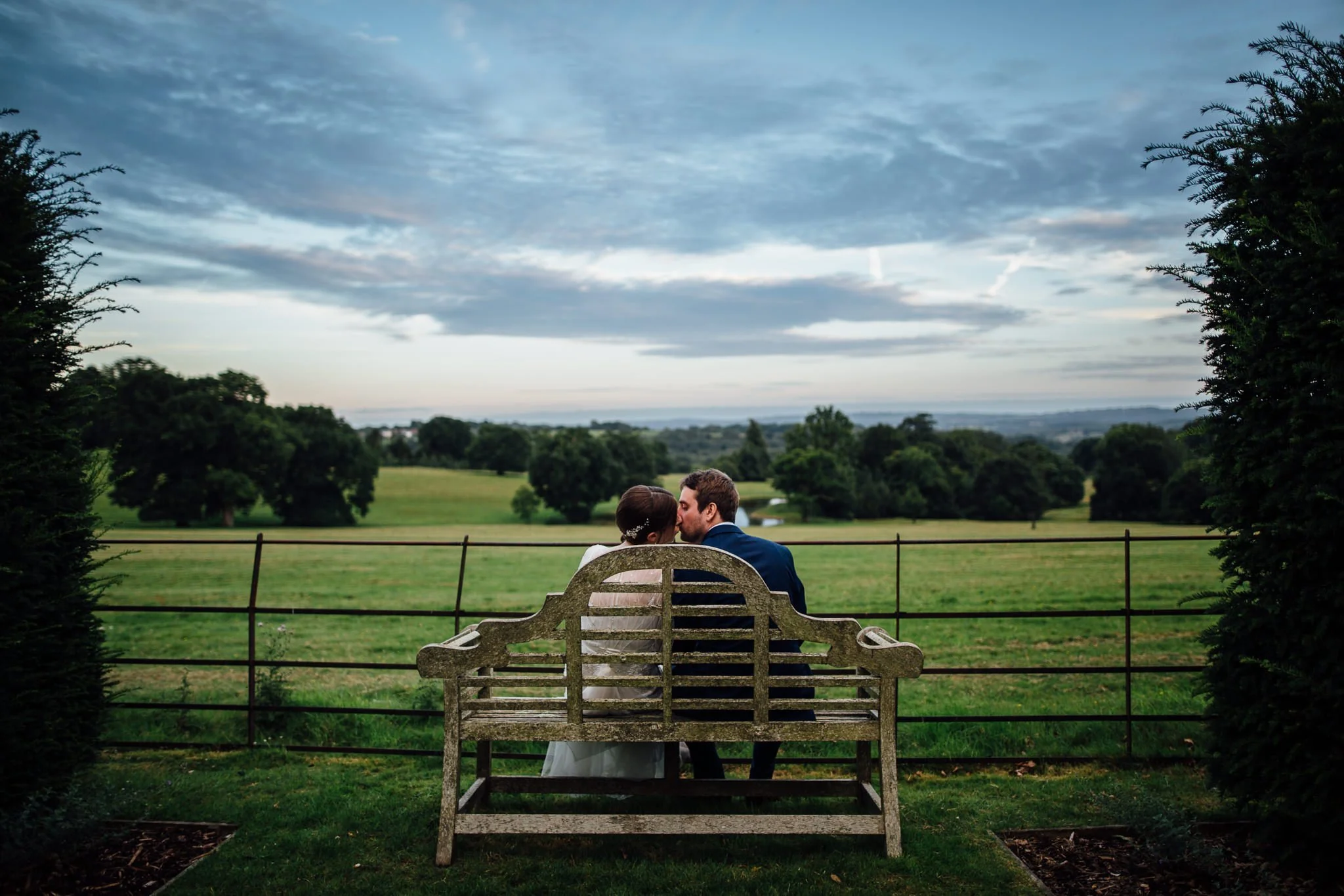  Bride and Groom kiss on a bench at  Wadhurst castle wedding venue 