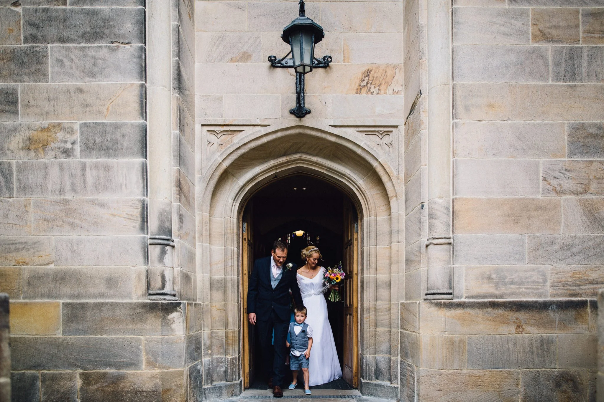  Bride and Groom walk out of All Saints Stand Church Whitefield with their son 