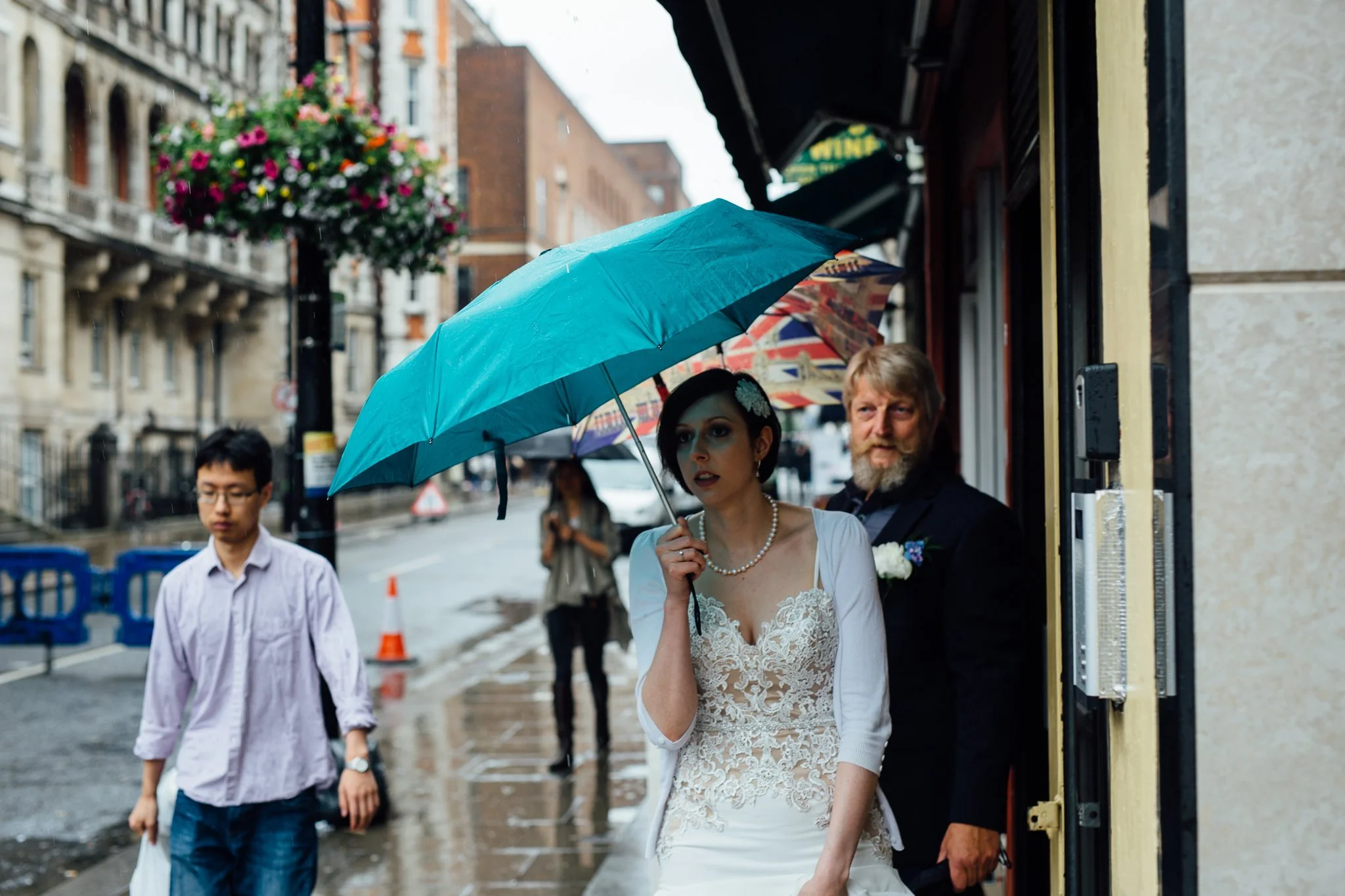  Bride walking down the street in Paddington hiding from the rain under an umbrella 