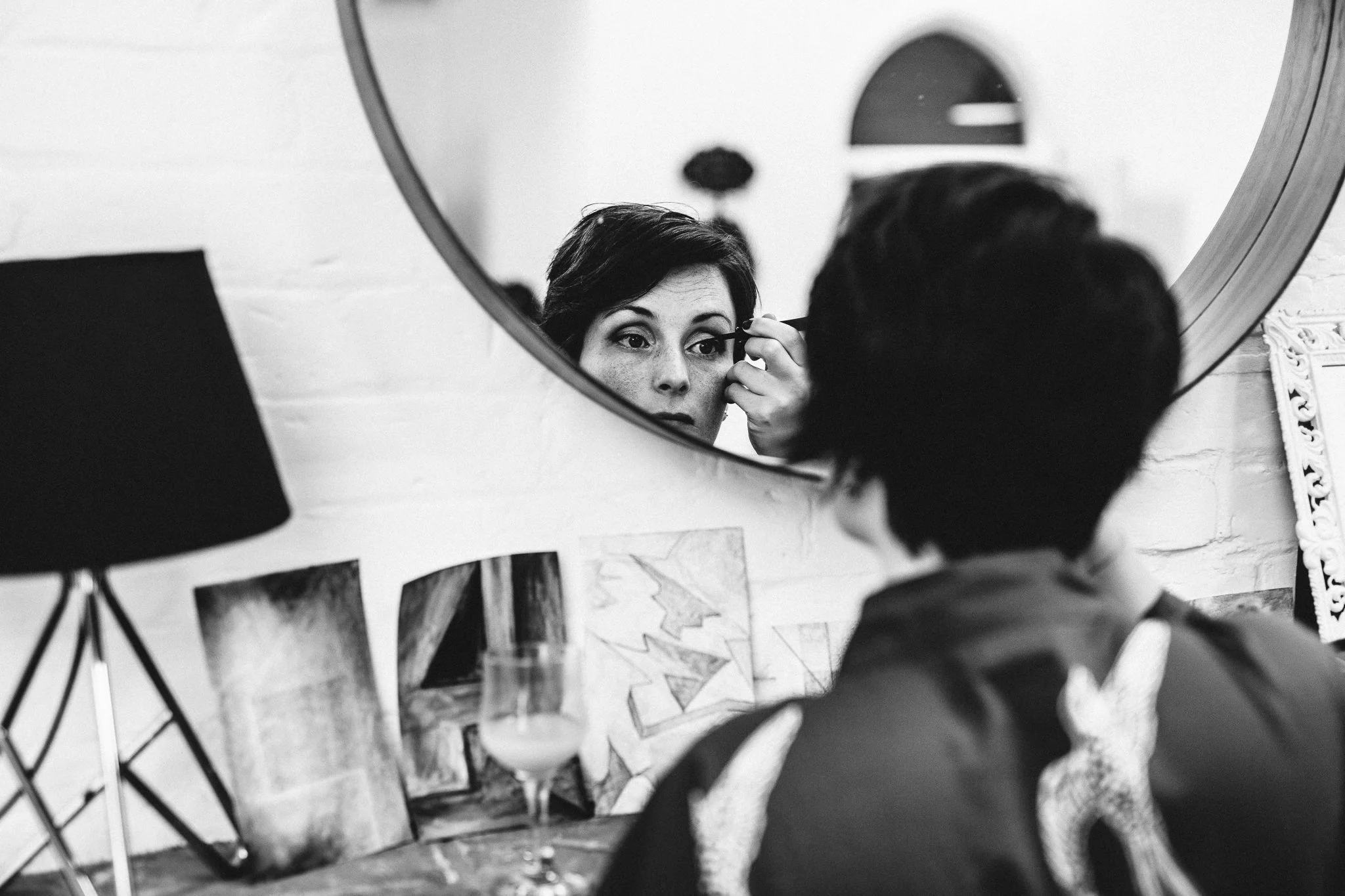  Bridesmaid looking in a mirror applying eye makeup 