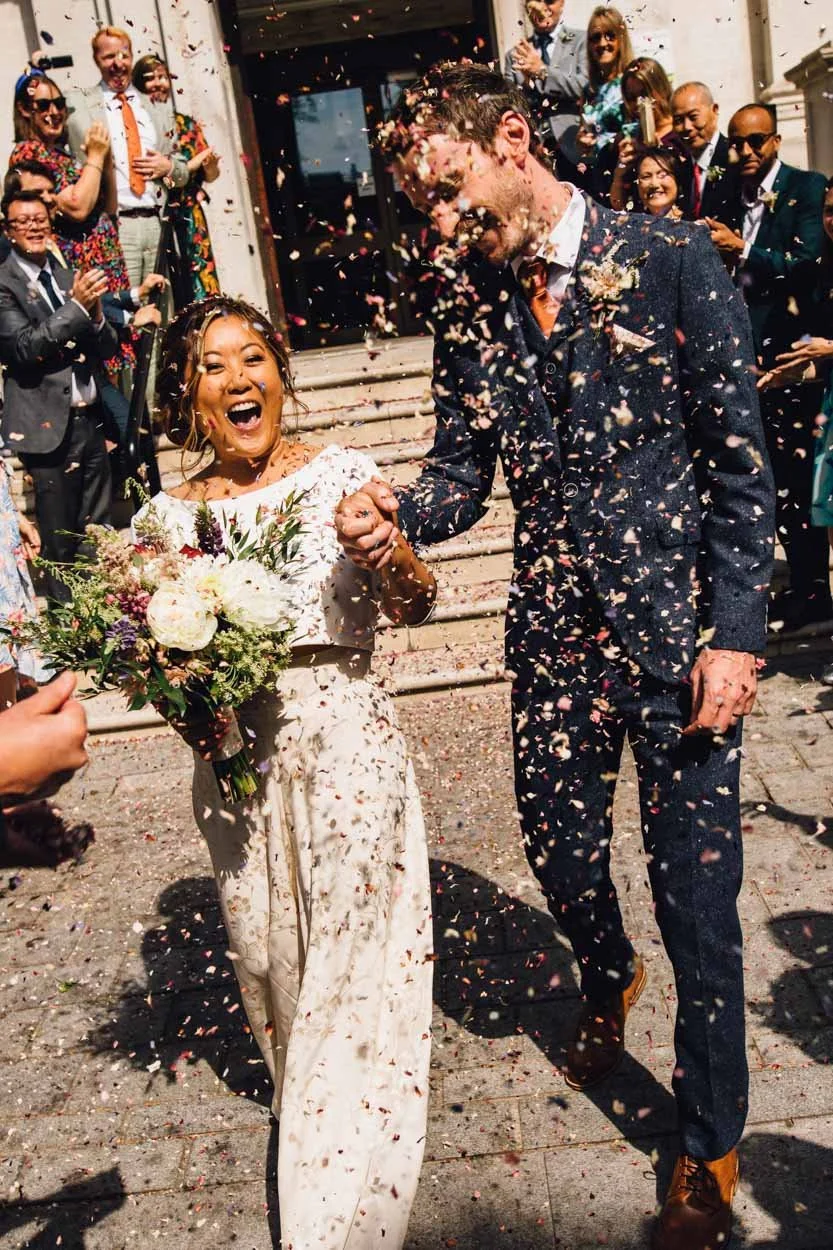 bride and groom smiling whilst having confetti thrown over them