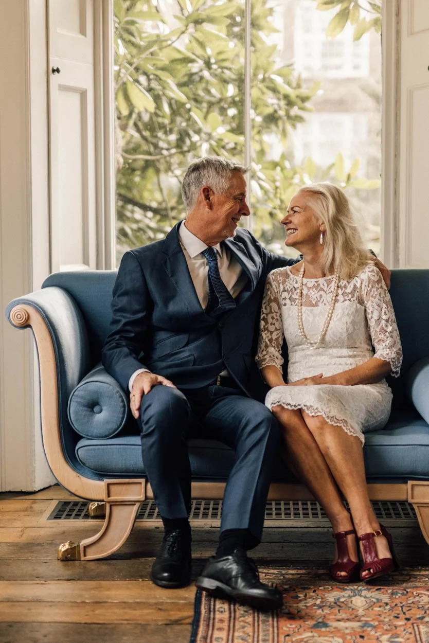 mature bride and groom sitting on a wooden framed sofa smiling