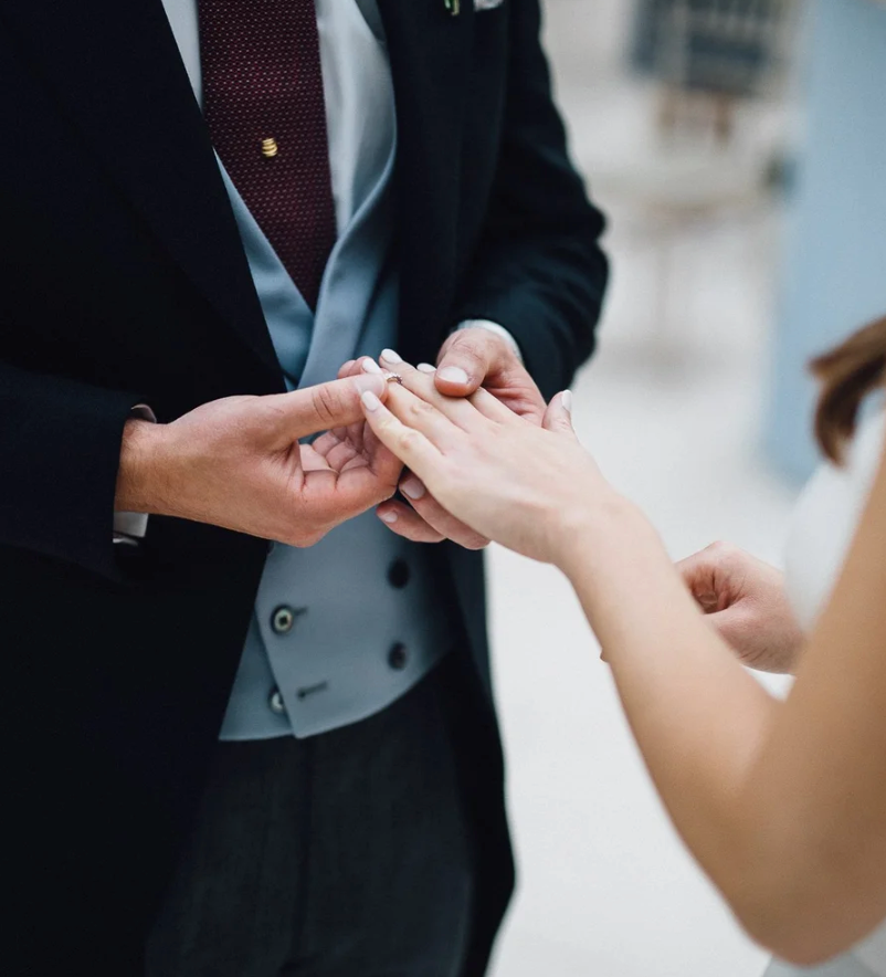 close up shot of groom wearing waistcoat placing ring on bride's finger by a west london wedding photographer