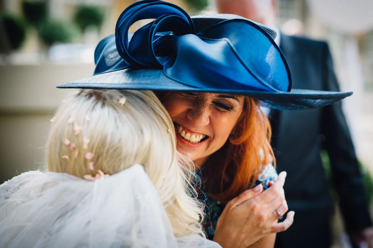 wedding guest wearing a blue hat hugging the bride