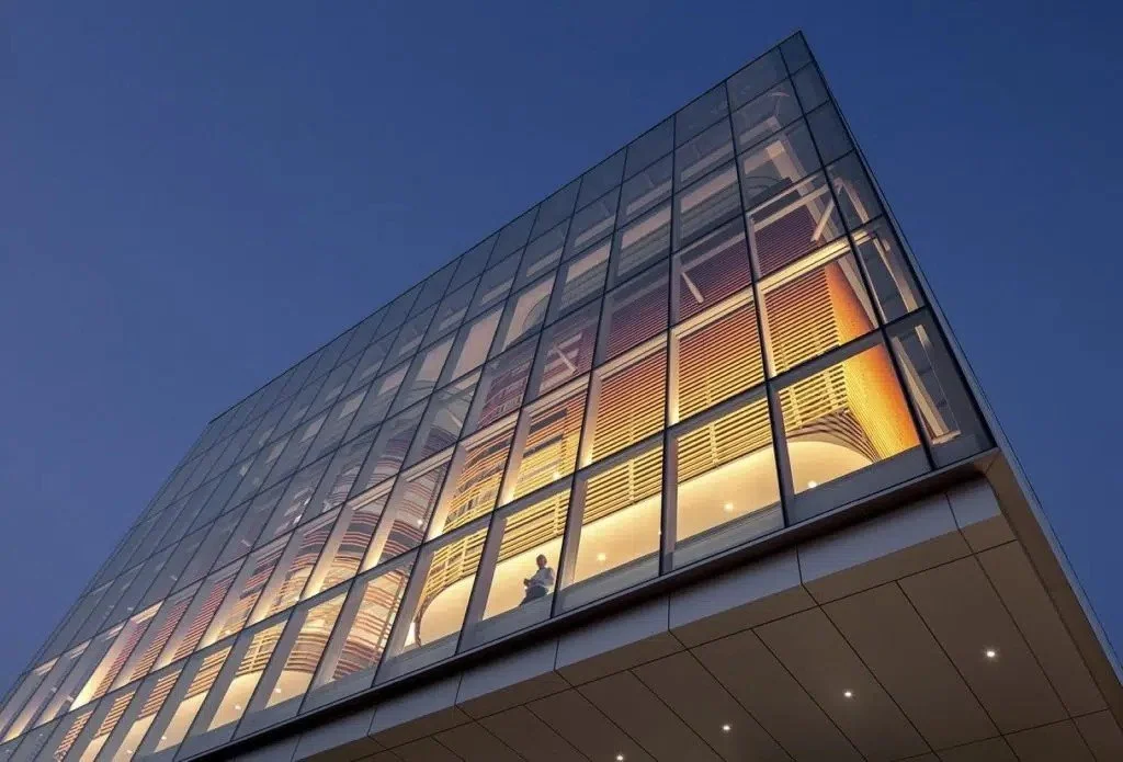 Low angle view of a modern glass building at night, with illuminated interior and a person visible through the glass.