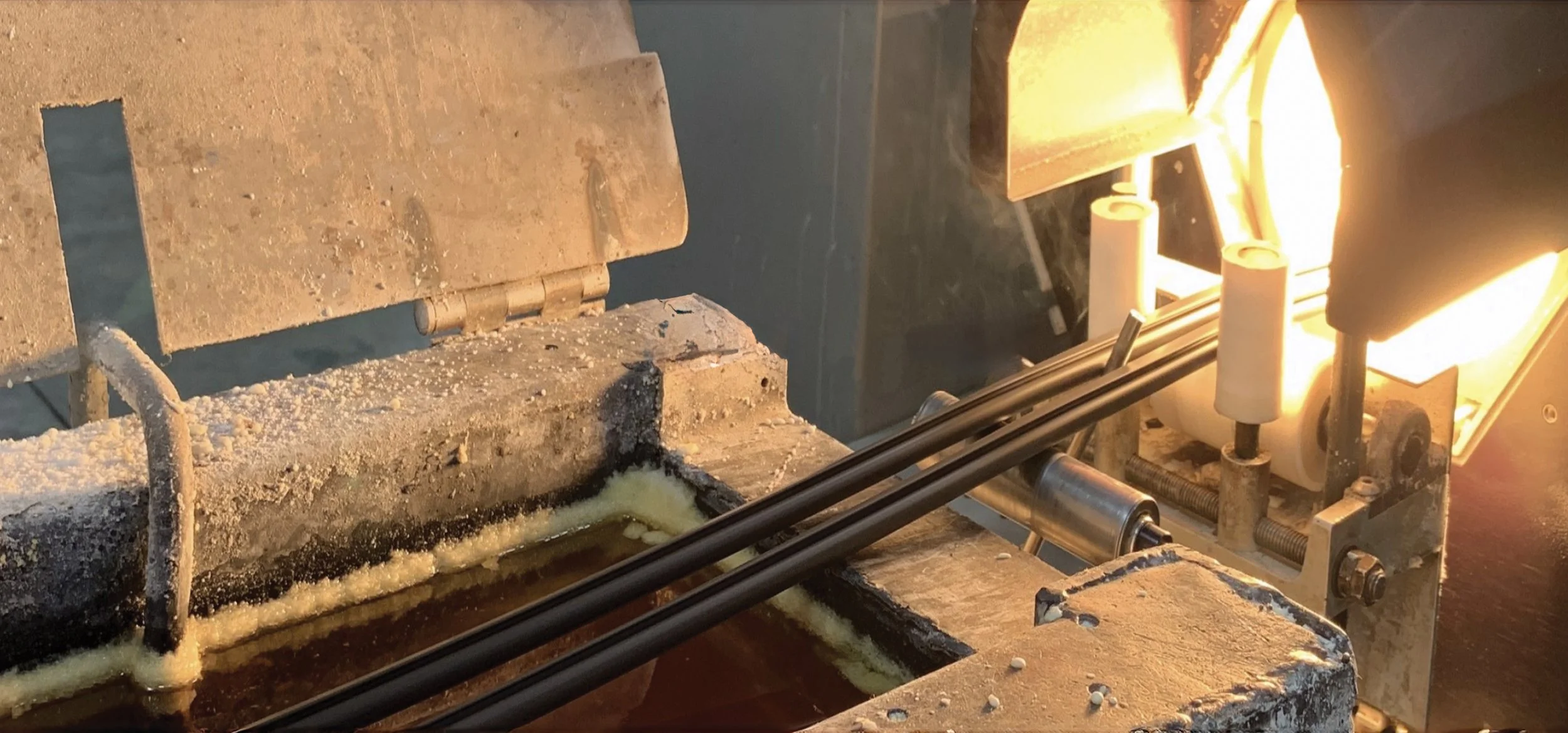 A metal machine with a heated section and rolling components, likely used for manufacturing or processing material, with bright lighting on the right side.