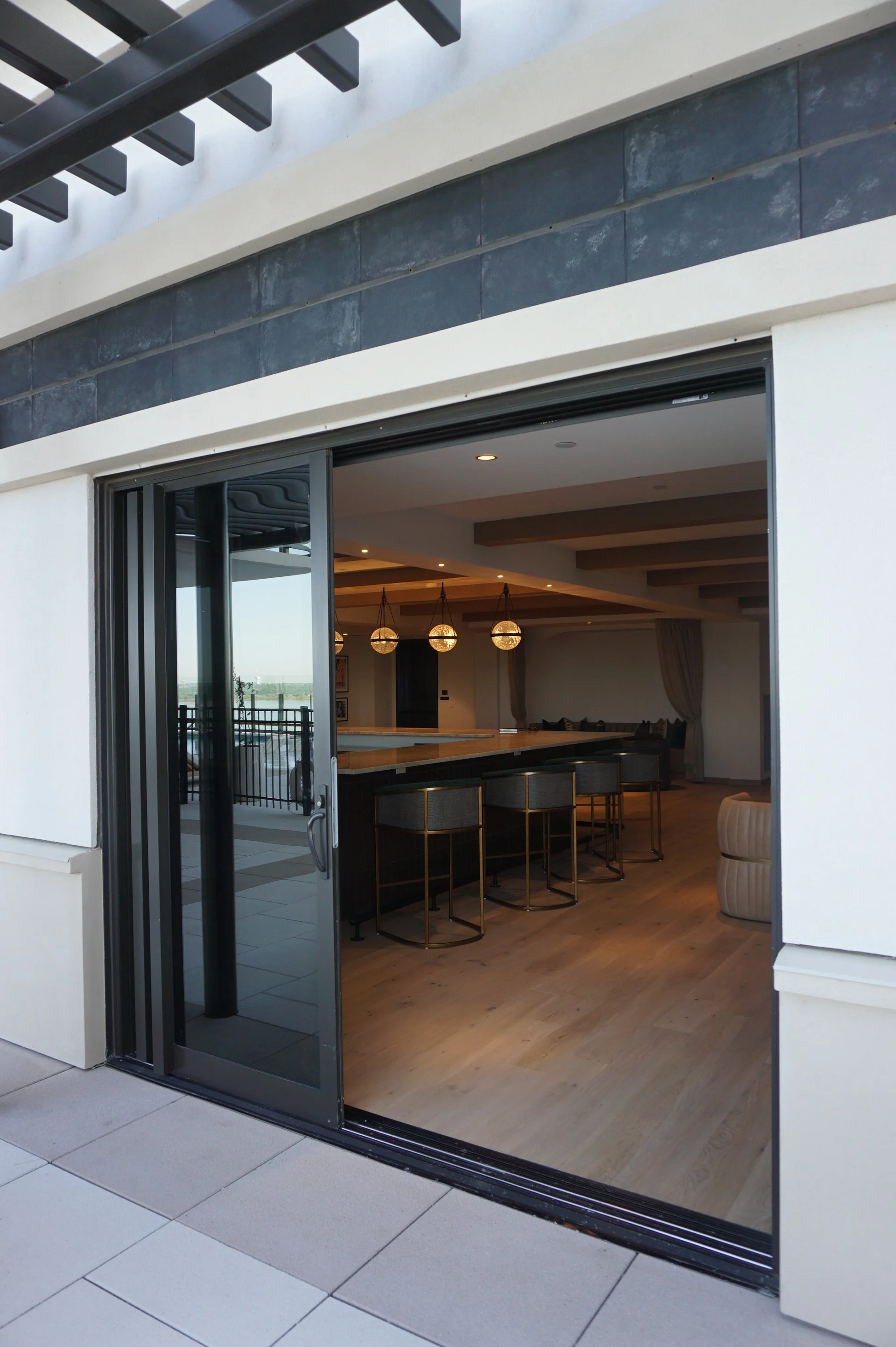Sliding glass door opening to an interior space with wooden flooring, barstools, and pendant lights in a modern home.