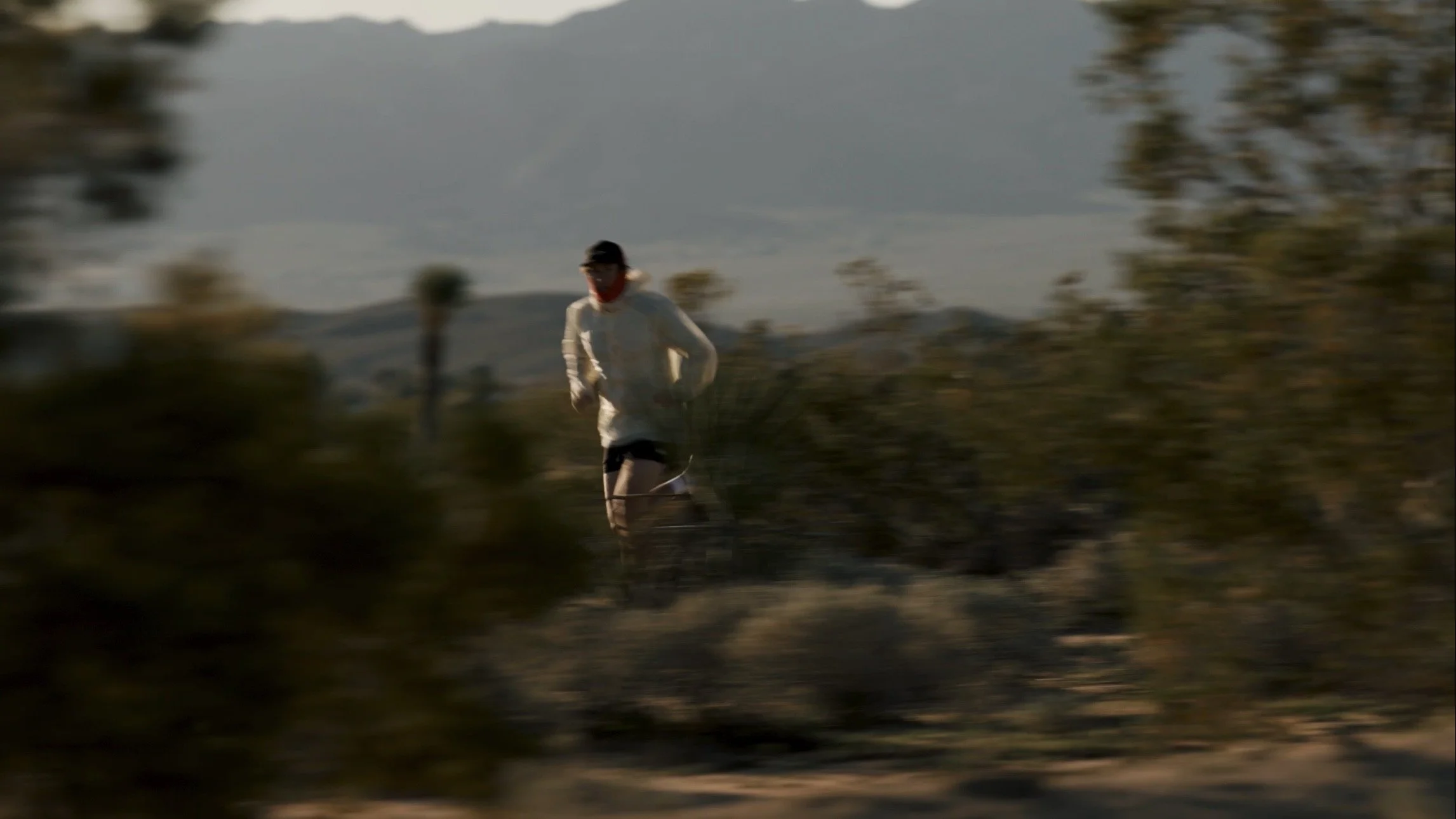 A person running outdoors in a natural setting during daylight, surrounded by trees and hills in the background.