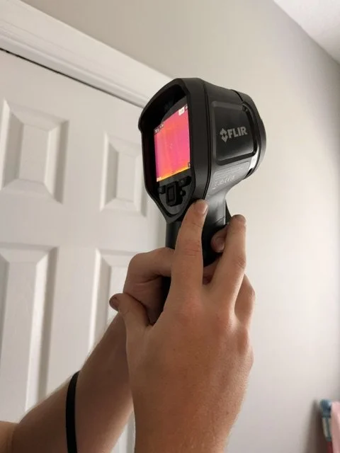 Person holding a FLIR infrared thermal camera pointed at the wall.