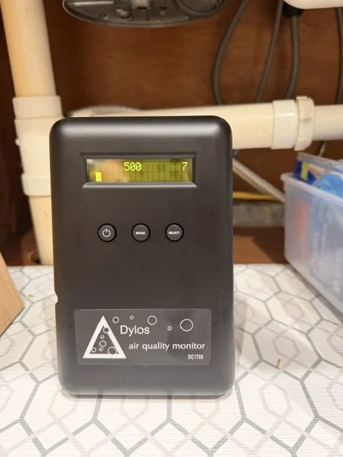 An air quality monitor on a tiled surface with a digital display showing a reading of 500 and a small yellow indicator.