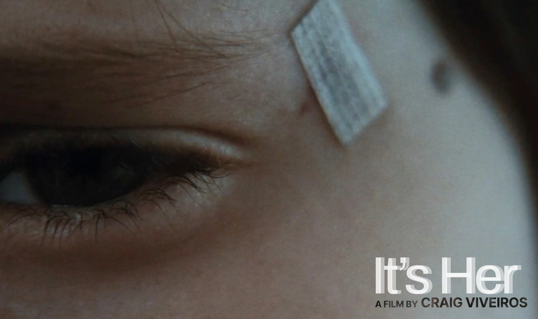 Close-up of a person's eye, with the area above the eye and a partially visible nasal prosthetic or scar. Text overlay says "It’s Her" and "A film by Craig Viveiros."