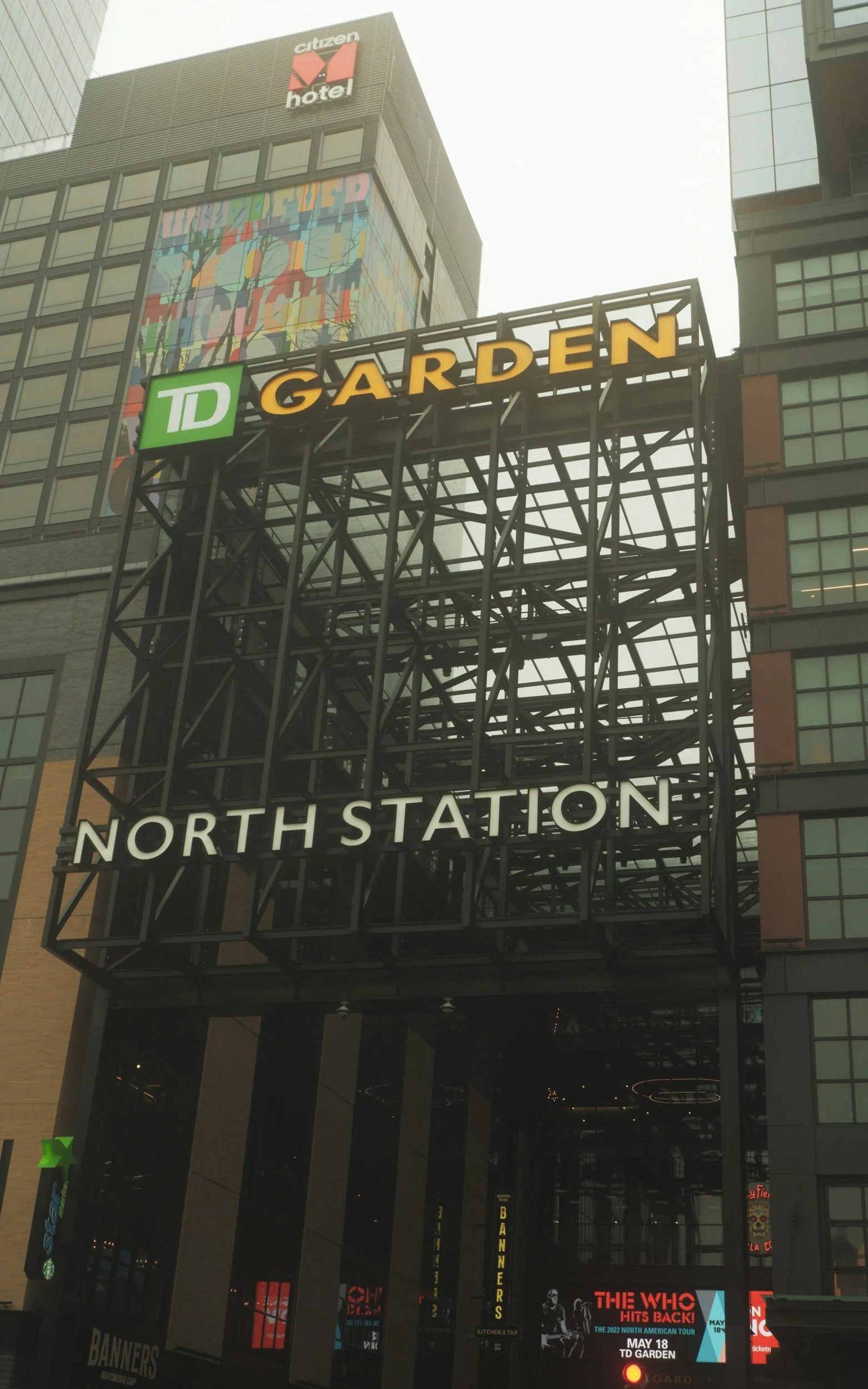 Tall buildings in an urban area with a large metal frame sign that reads 'TD GARDEN' and 'NORTH STATION', surrounded by advertisements and digital screens.